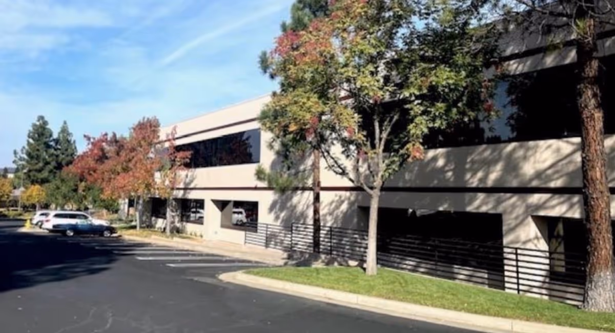 Exterior view of a beige two-story building with parking and trees along the front.