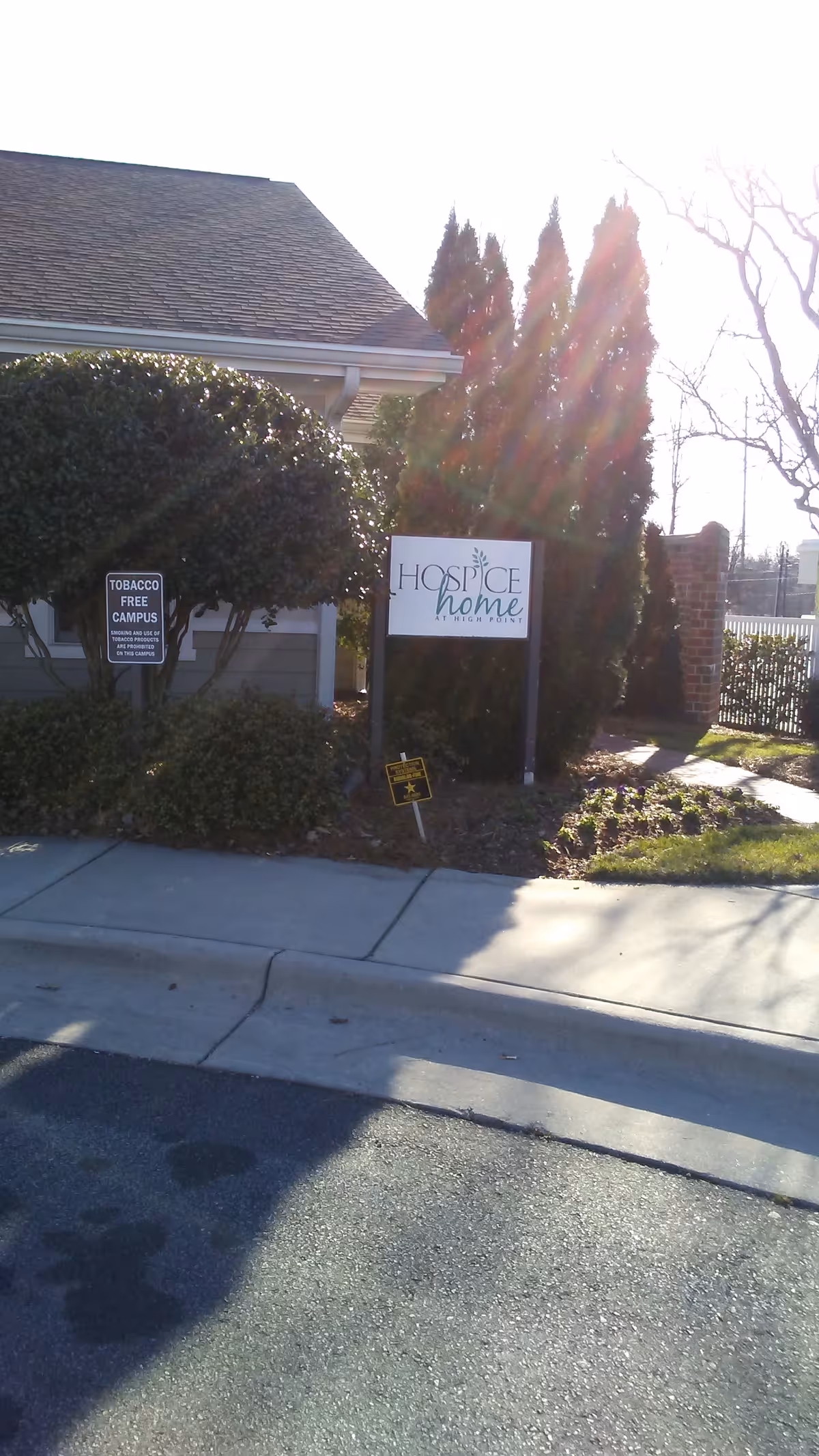 Exterior view of a hospice entrance with shrubs, a sidewalk, and a sign
