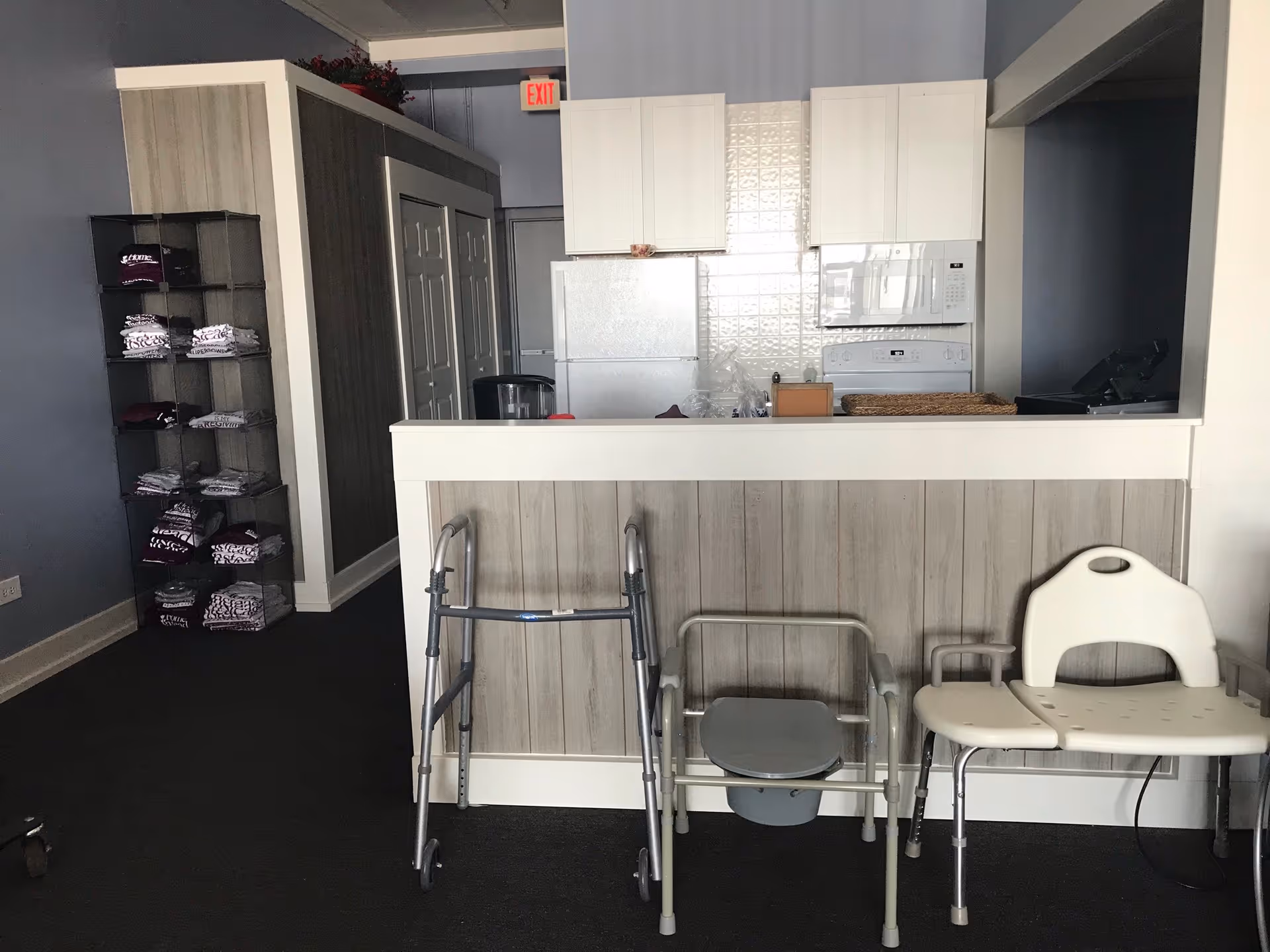 Small kitchen area in a senior facility with white cabinets, fridge, microwave, and walkers nearby.