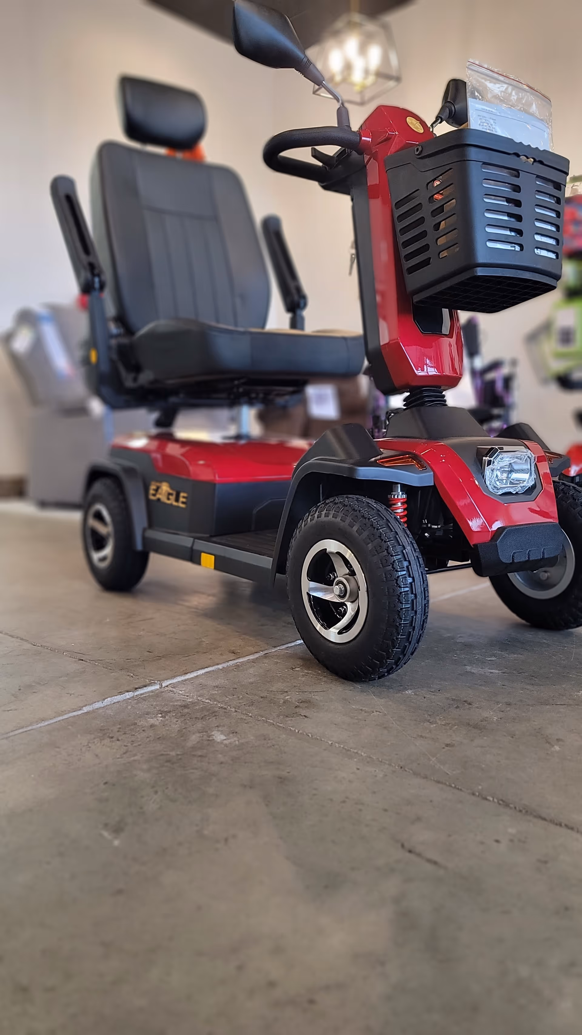 Red mobility scooter with a front basket sits indoors on a showroom floor.