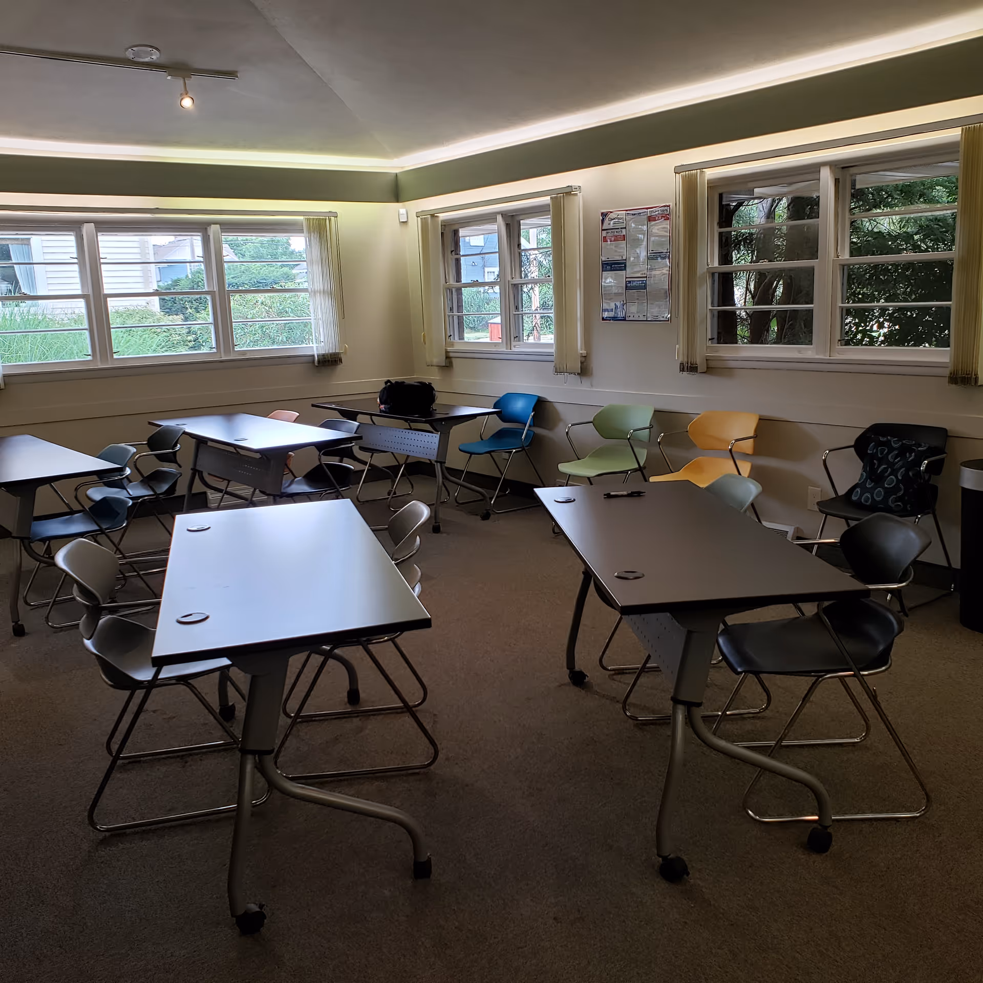 Sunlit classroom-style activity room with multiple tables and colorful chairs.