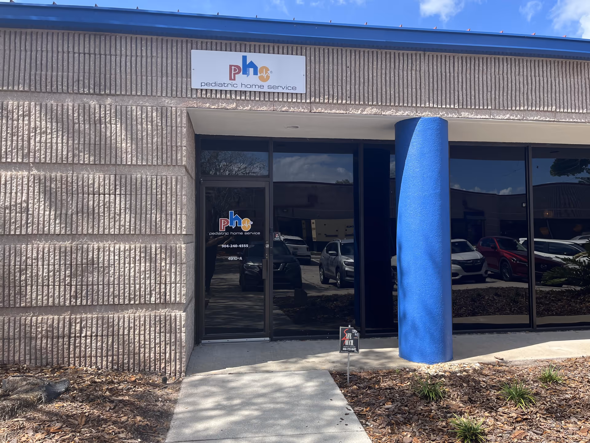 Exterior view of a pediatric home service facility with glass doors and blue column.