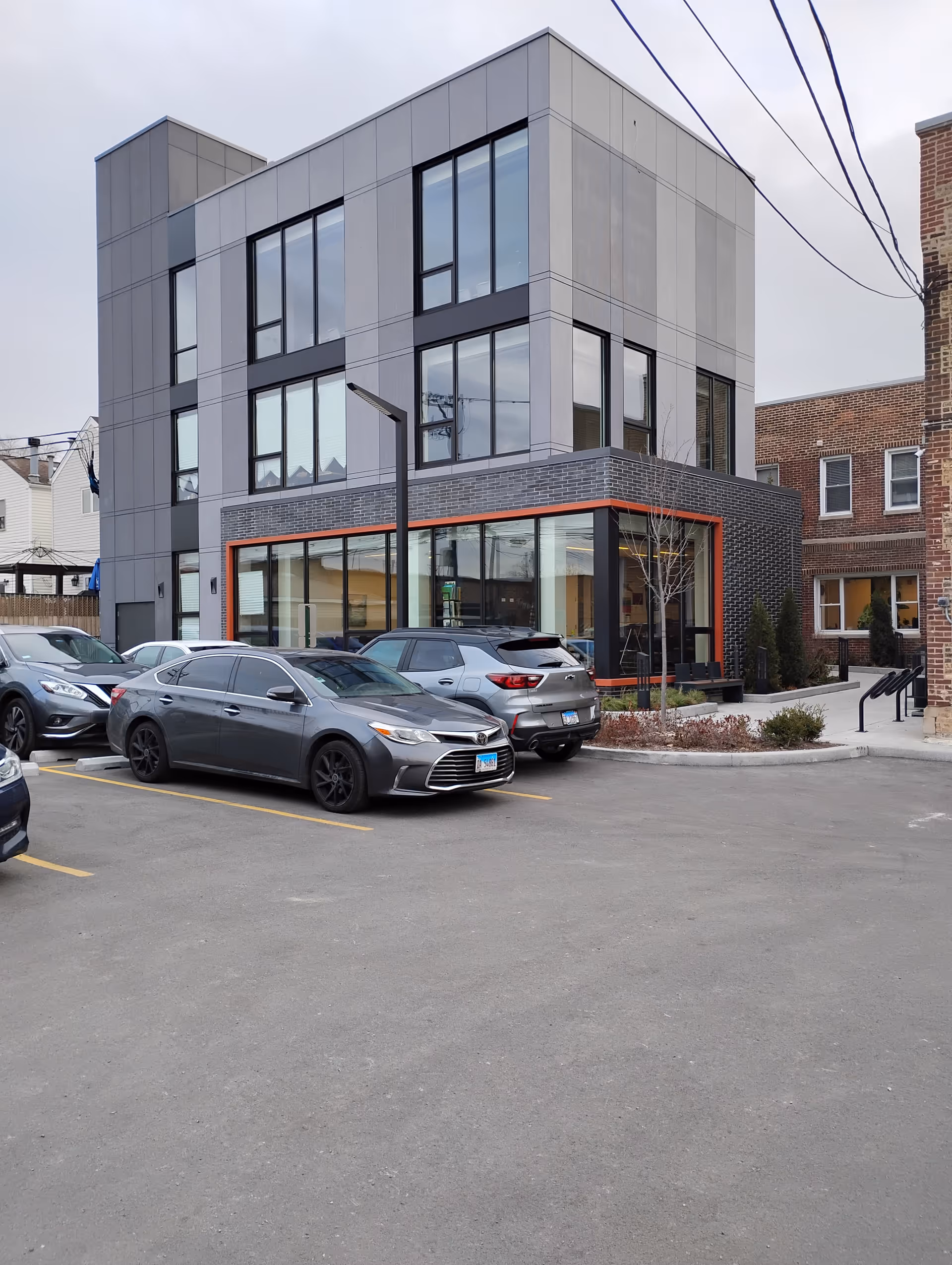 Modern multi-story building with large windows and a parking lot in front.