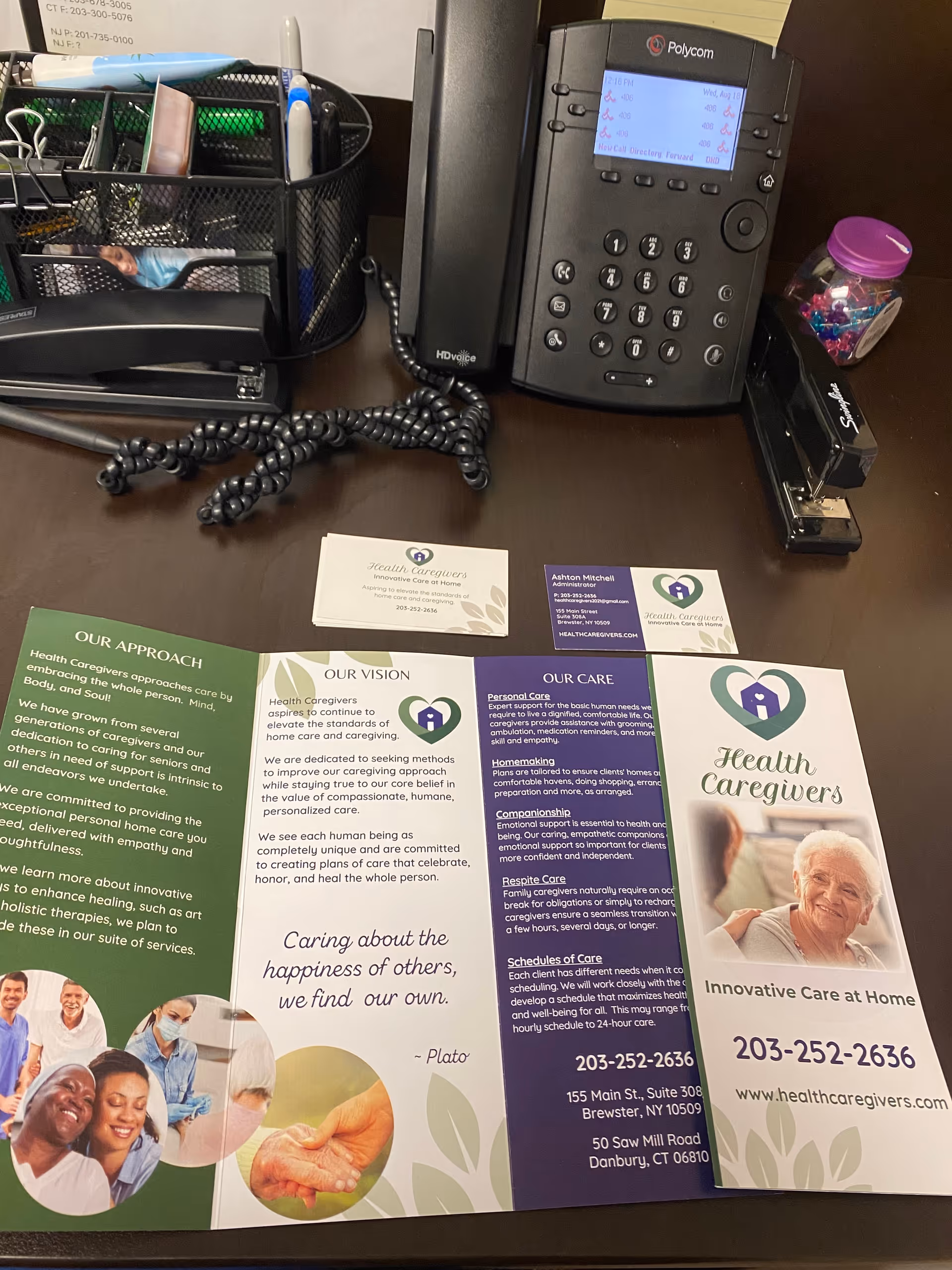 Office desk with a Polycom phone, supplies, and Health Caregivers brochures.