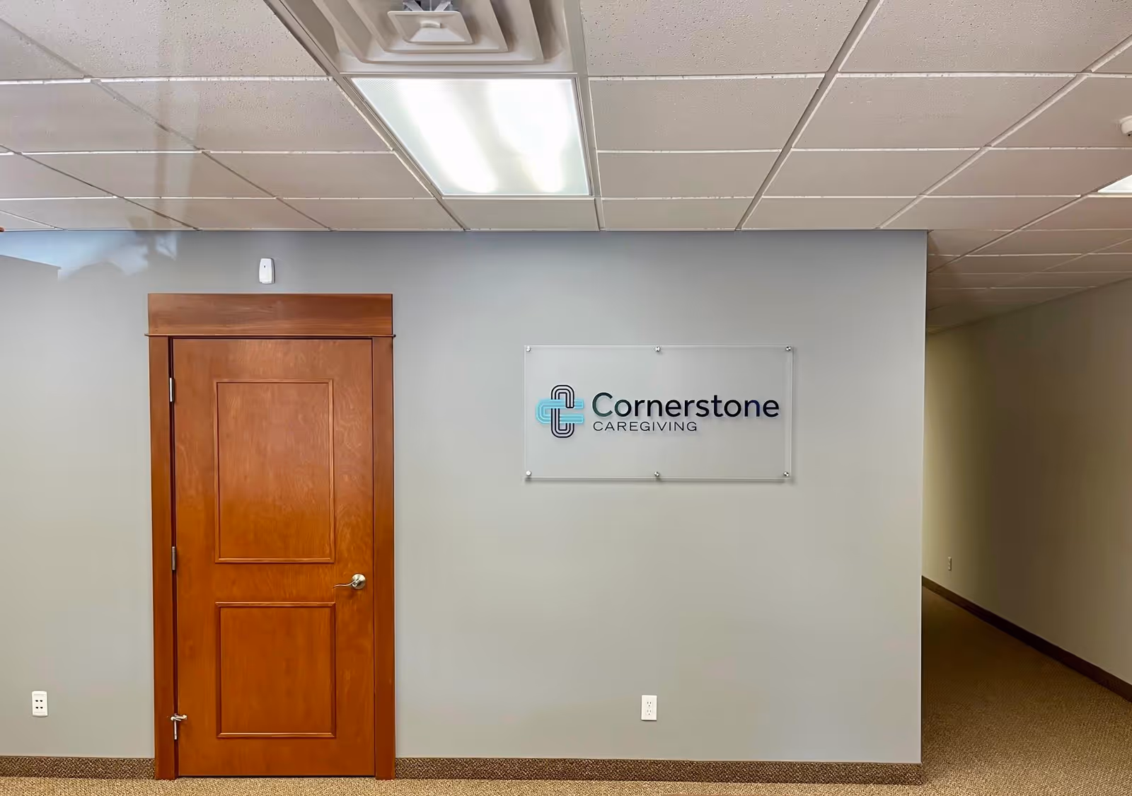 Interior hallway featuring a wooden door and Cornerstone Caregiving sign on the wall.