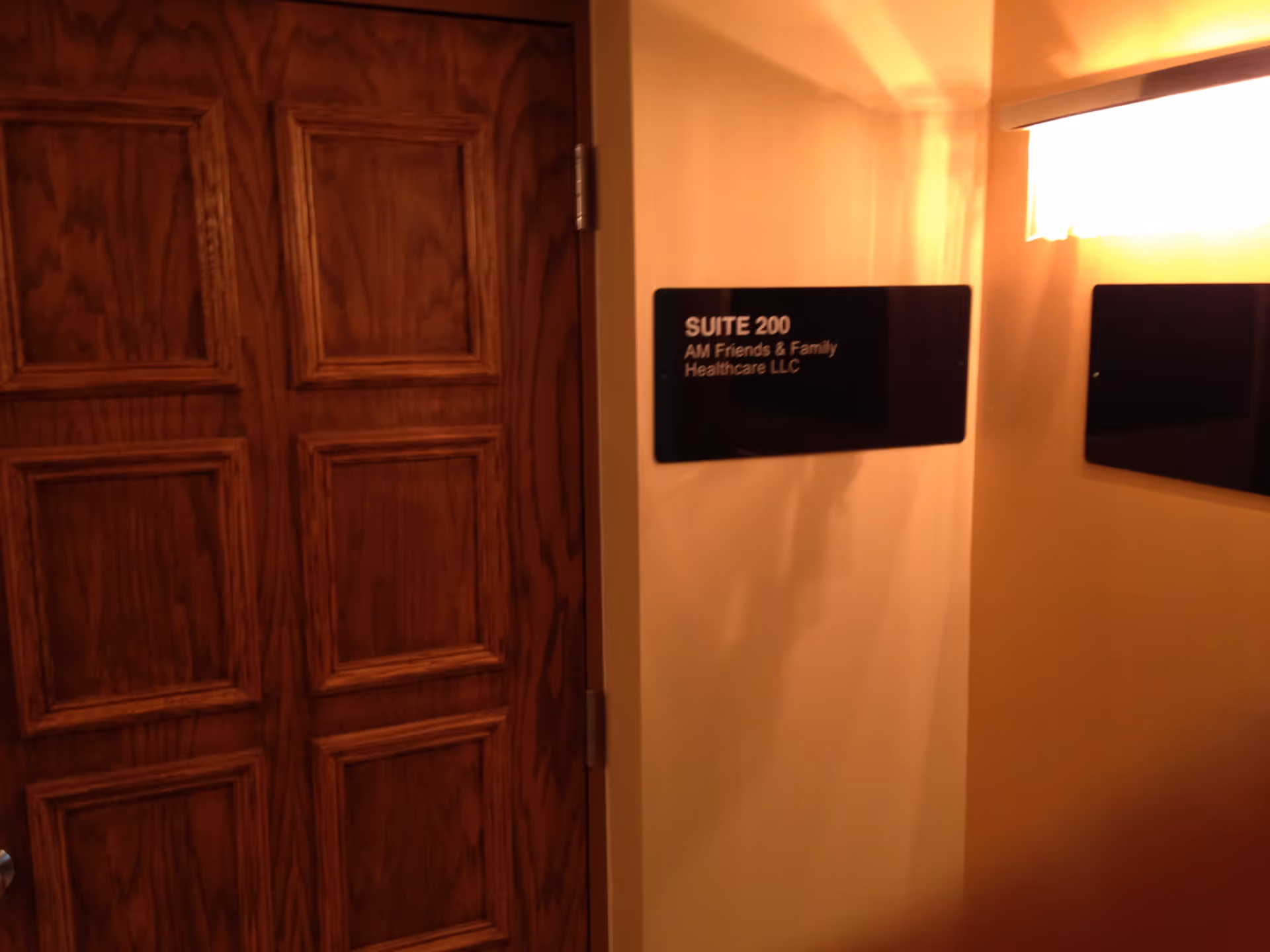 Wood-paneled double doors on left; hallway plaque reads 'SUITE 200 AM Friends & Family Healthcare LLC'.