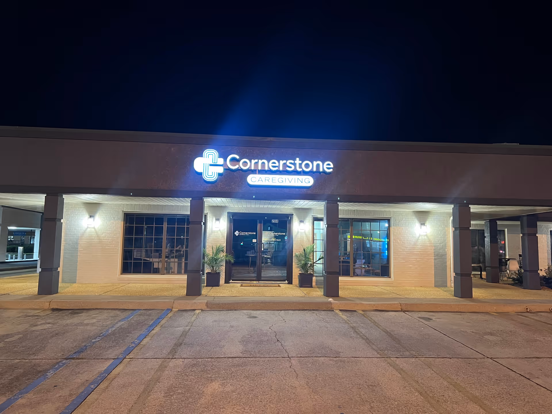 Night exterior of Cornerstone Caregiving building with illuminated sign and glass entrance.