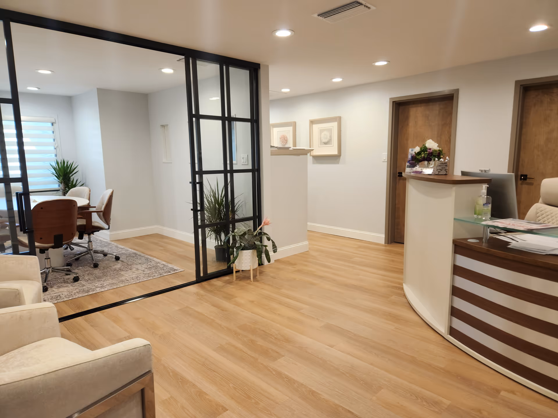 Modern reception area with curved desk, glass divider, seating, and plants in a senior facility.
