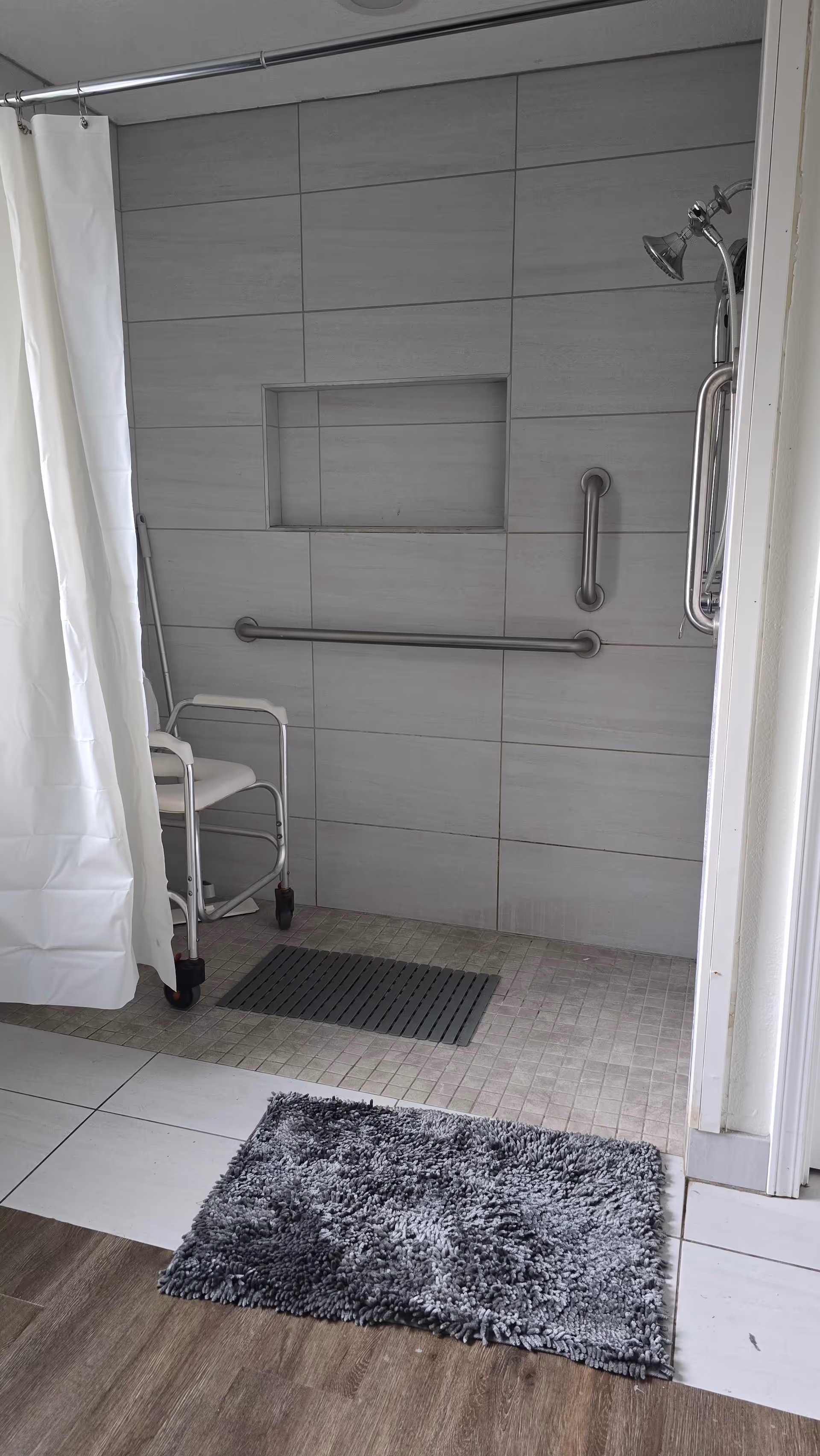 Accessible shower area with grab bars, a shower seat, and curtain in a bathroom.