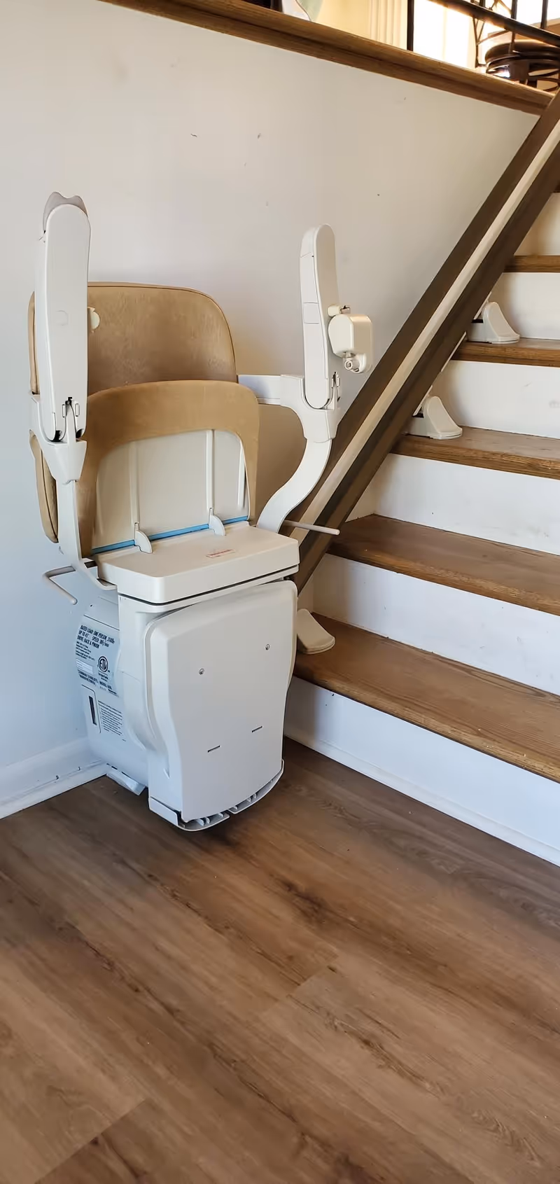A stairlift chair installed on a wooden indoor staircase beside a wall.