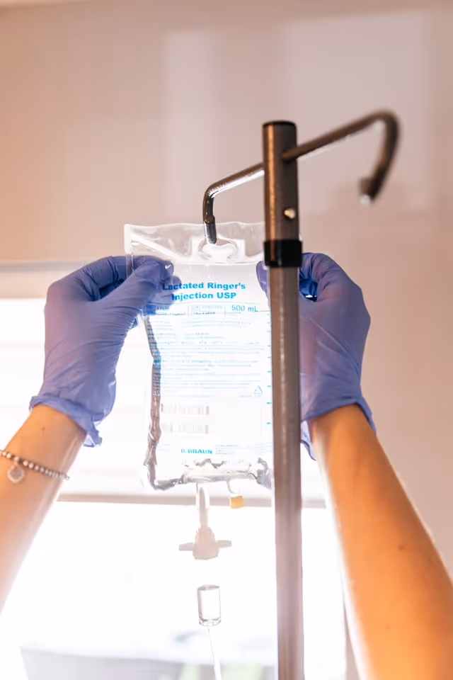 Gloved hands adjust an IV bag on a stand indoors.