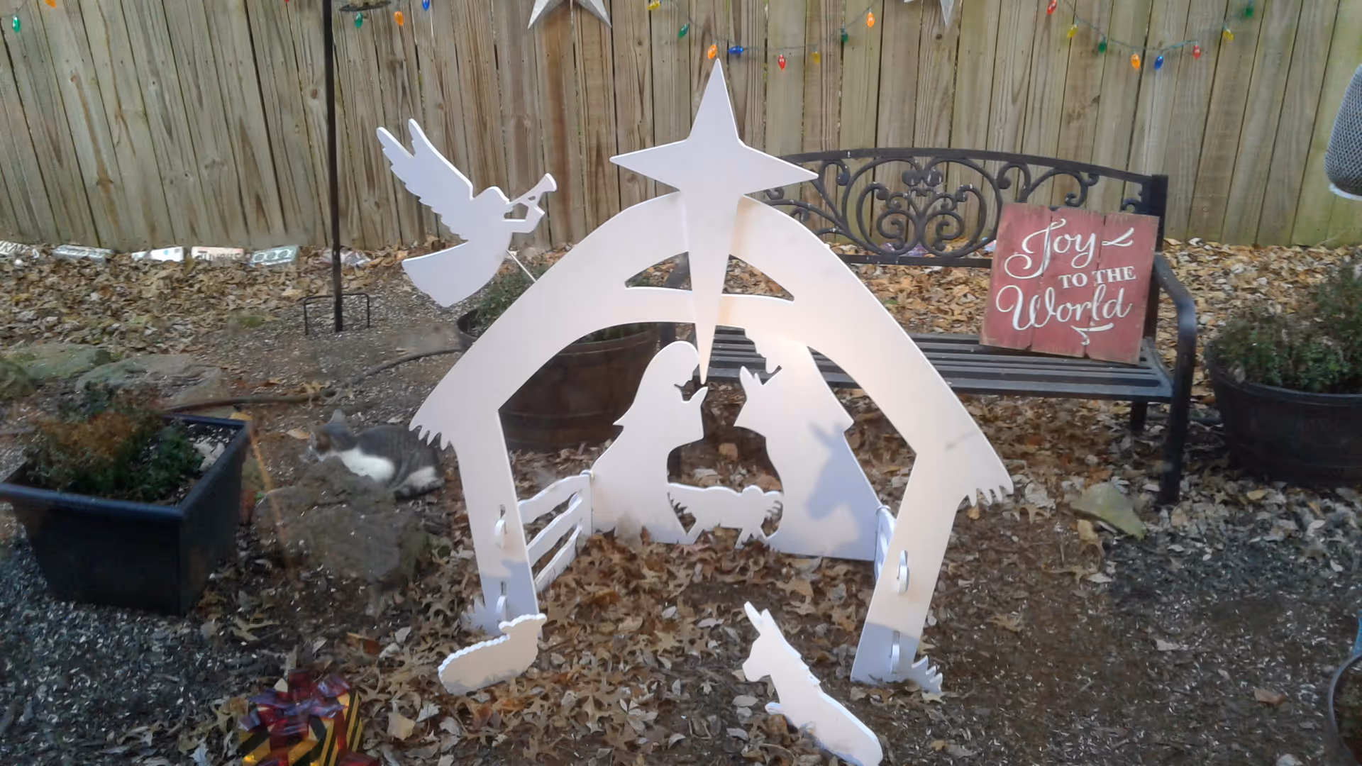 Outdoor yard scene featuring a white nativity cutout, a bench with Joy to the World sign.