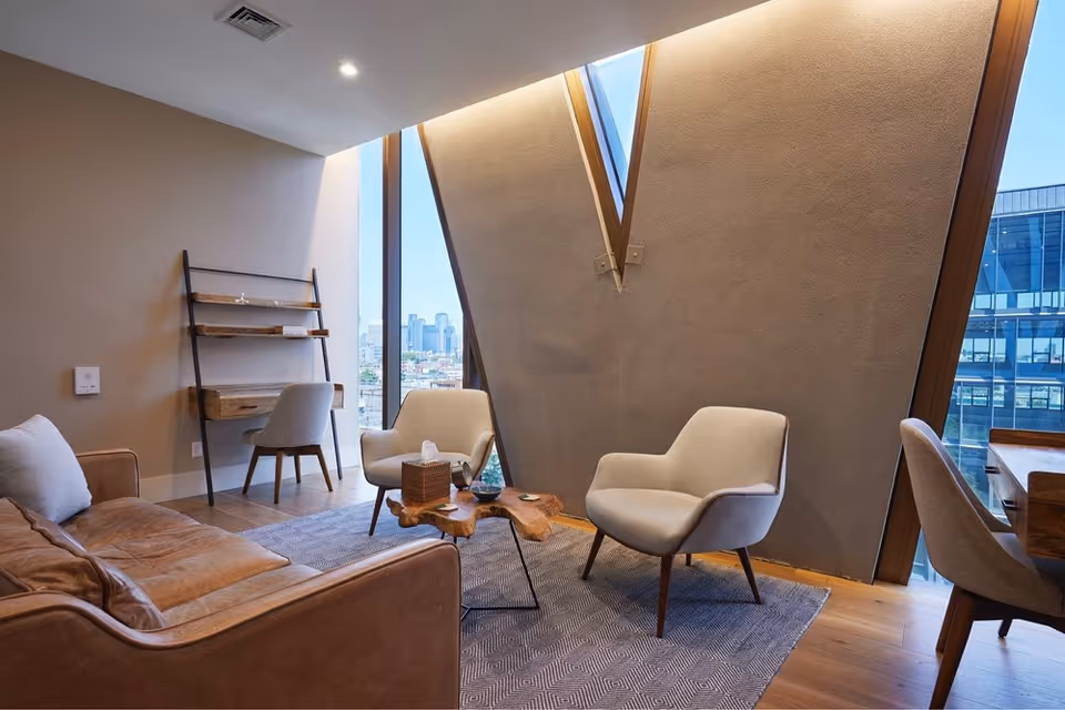 A modern senior living lounge with leather sofa, chairs, wooden coffee table, and large windows.