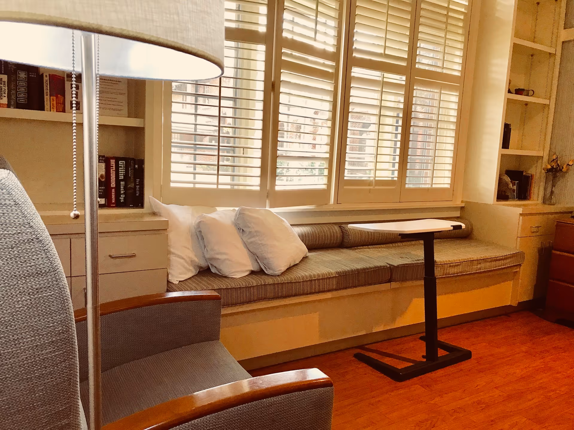Sunlit window seat with cushions and a small table in a cozy living room.