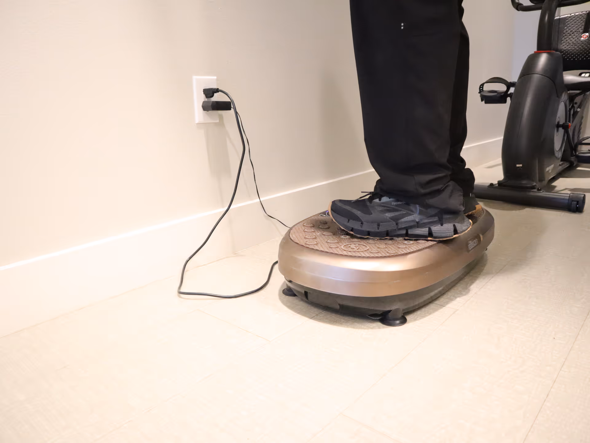 Person stands on a circular balance platform plugged into an outlet in a rehab room