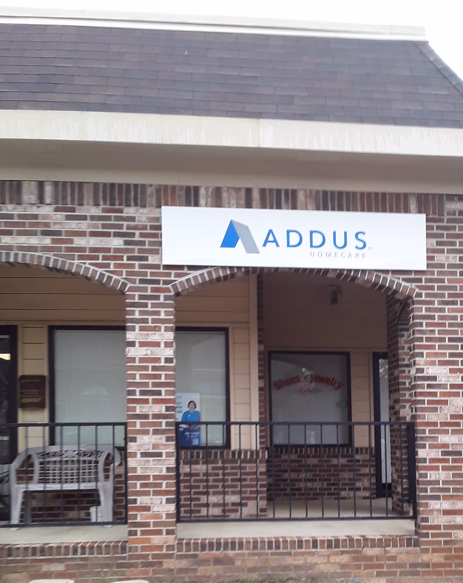 Brick storefront with Addus HomeCare sign and porch railing at the entrance.
