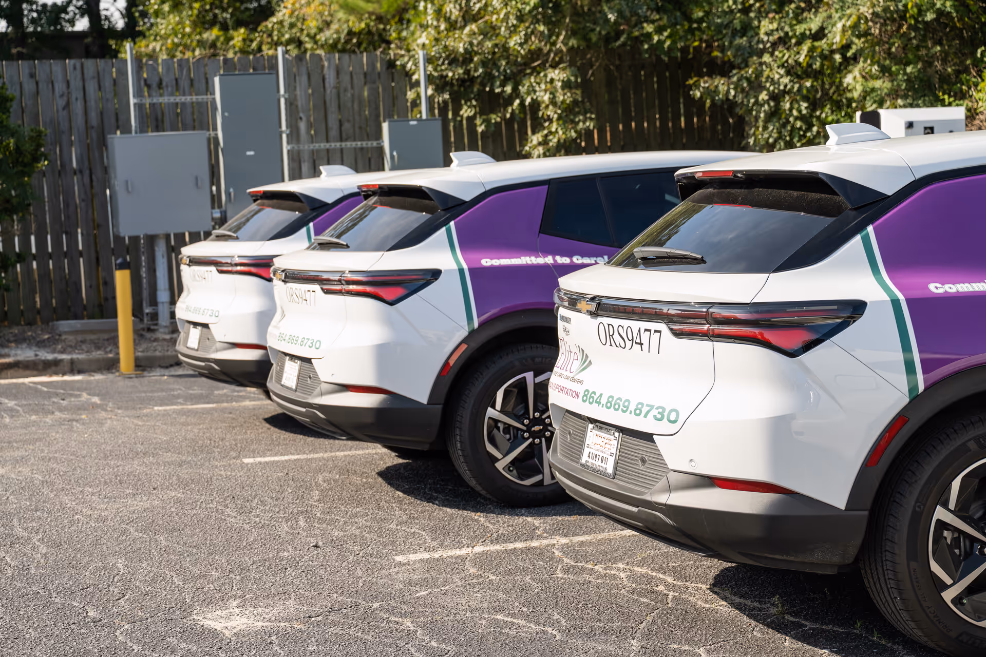 Row of white and purple shuttle vans parked in a lot outside Elite Home Care Centers.