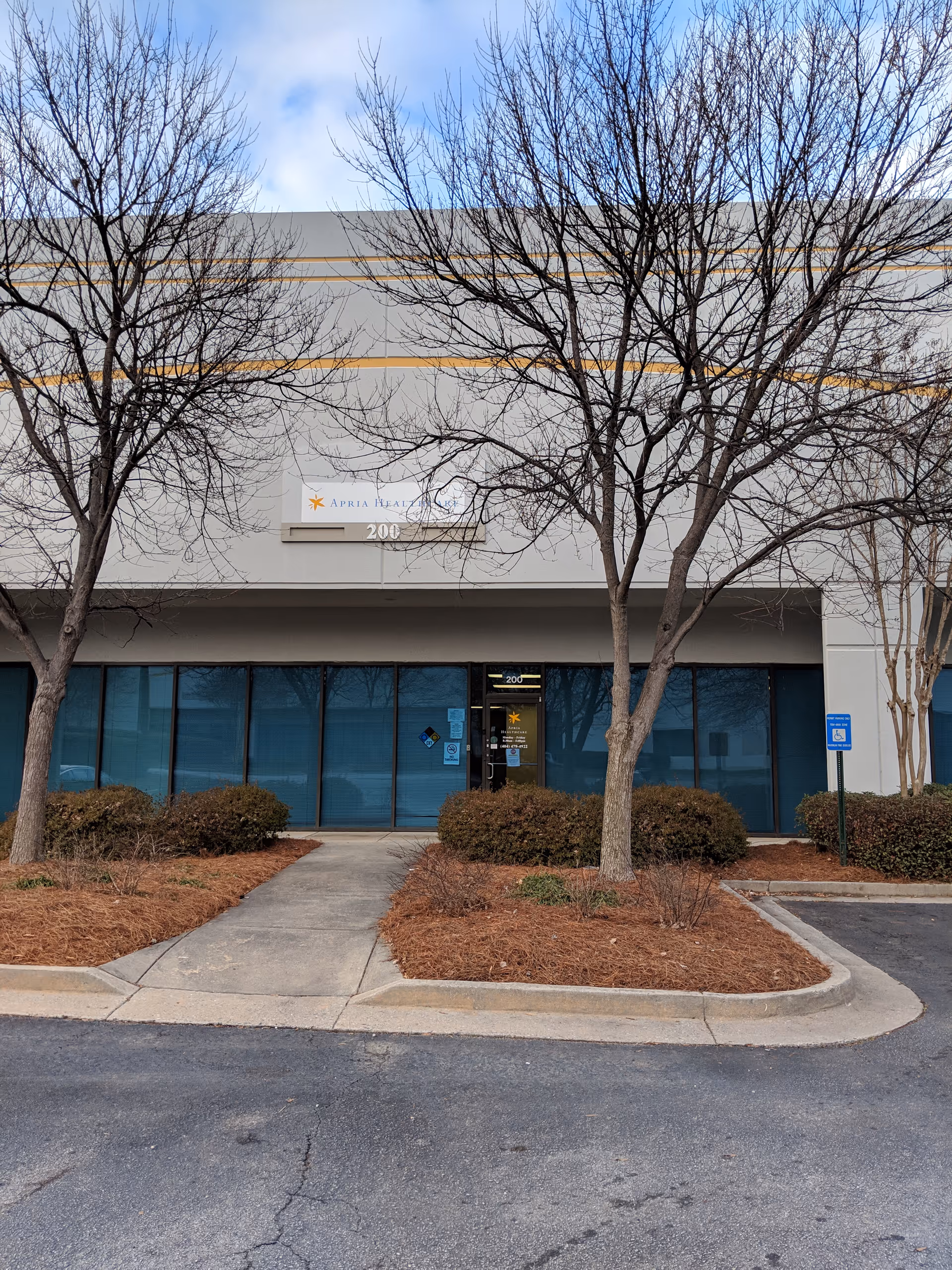 Front view of Apria Healthcare building entrance with glass doors and leafless trees.
