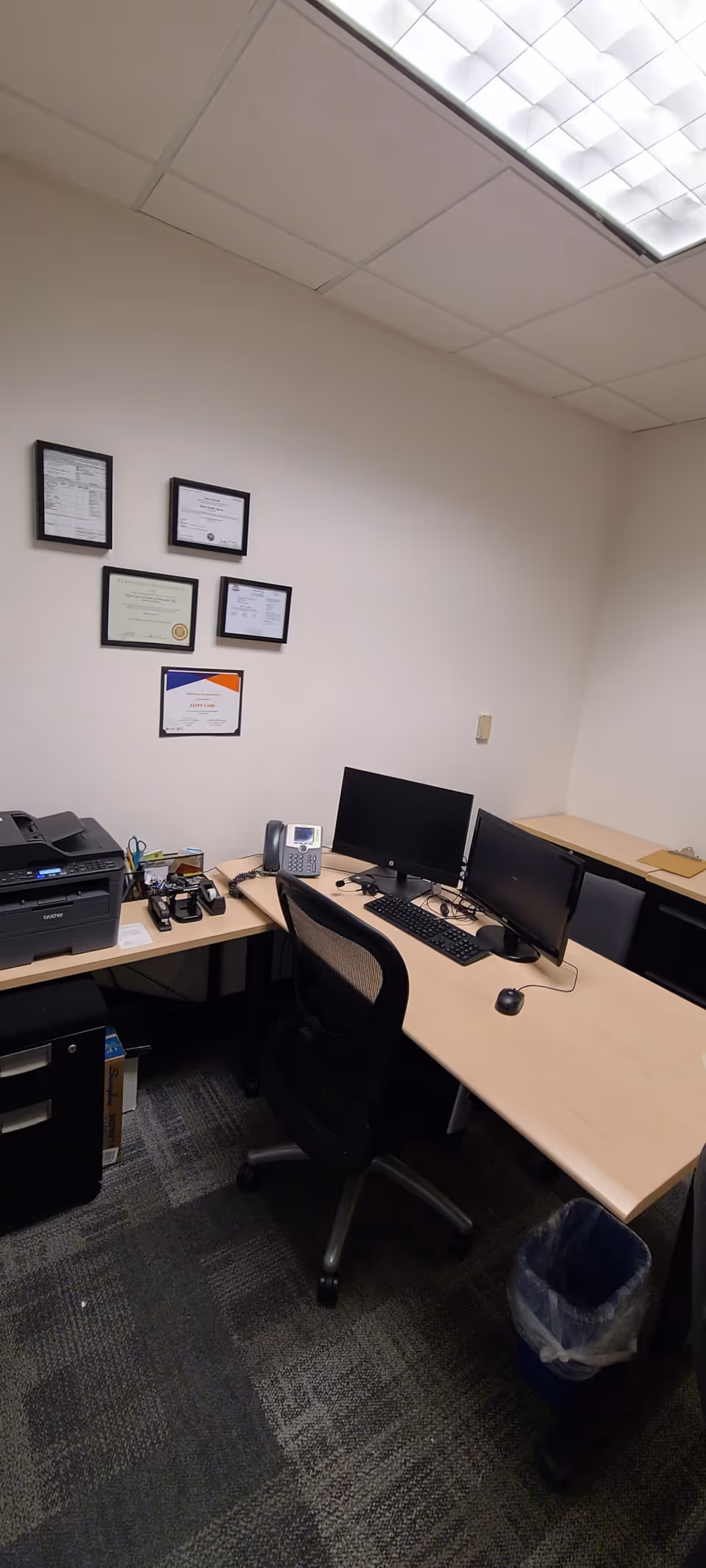 Office area with desks, dual computer stations, printer, phone, and framed certificates.