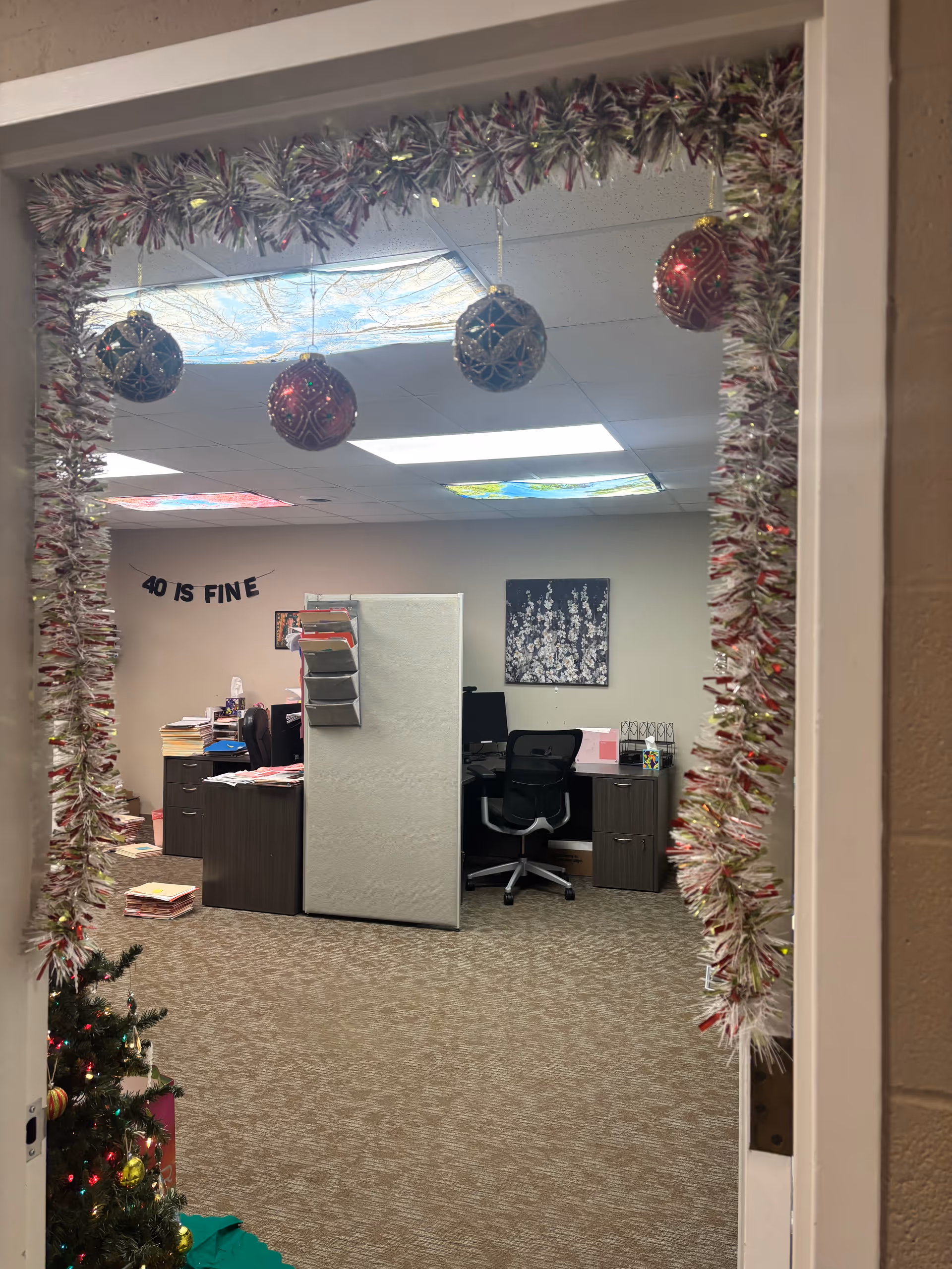 Office workspace with desks and cubicles framed by festive holiday garlands.