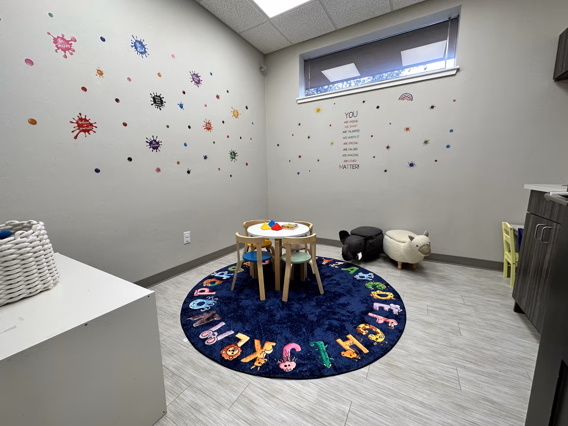 Small children's activity room with round alphabet rug, table, chairs, and wall decals.