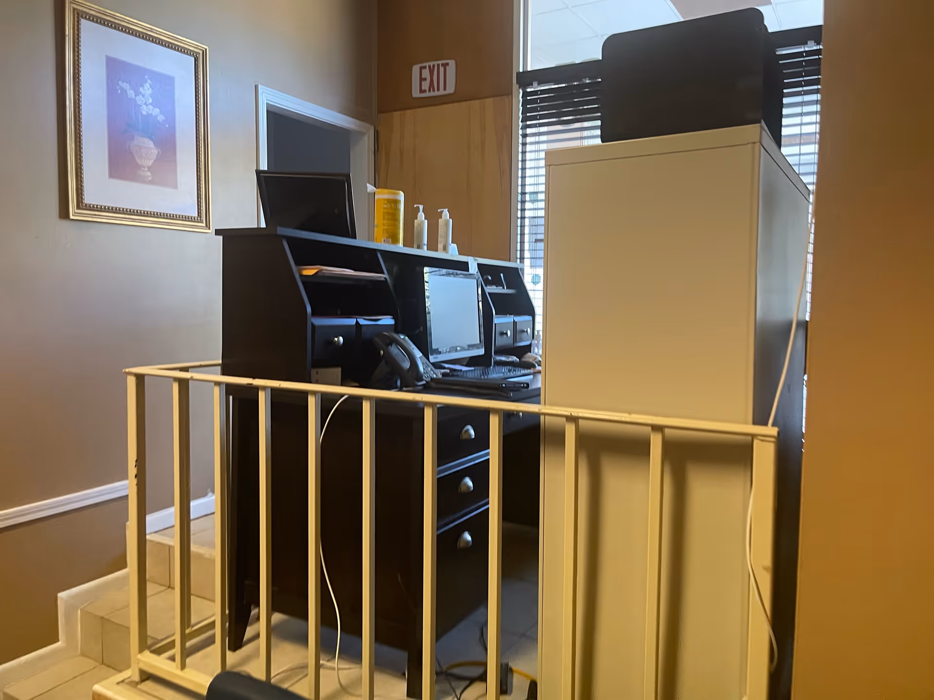Office workstation with computer, printer, and supplies beside a railing in a hallway.
