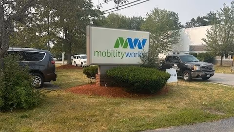 Exterior view of MobilityWorks sign in front of building with parked cars.