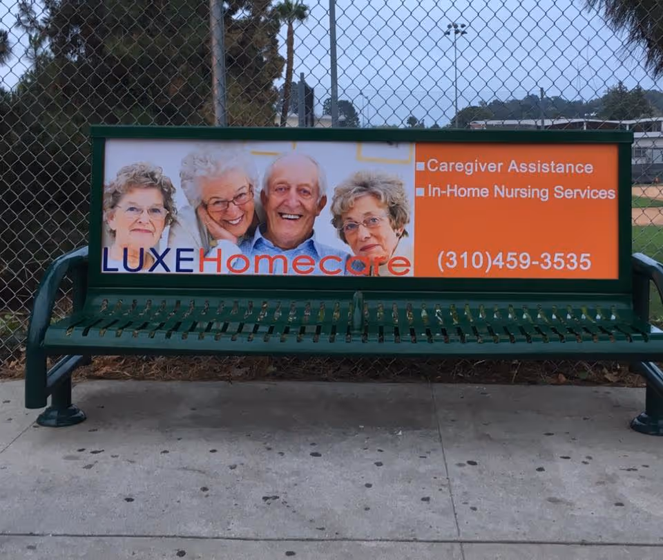 Green outdoor bench with Luxe Homecare advertisement sign featuring smiling elderly people.
