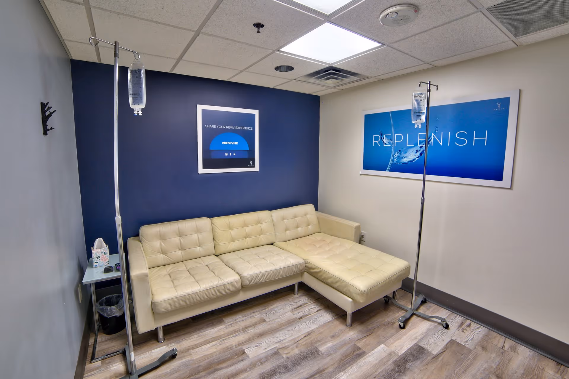 IV therapy room with beige sectional sofa, IV stands, and blue wall art.