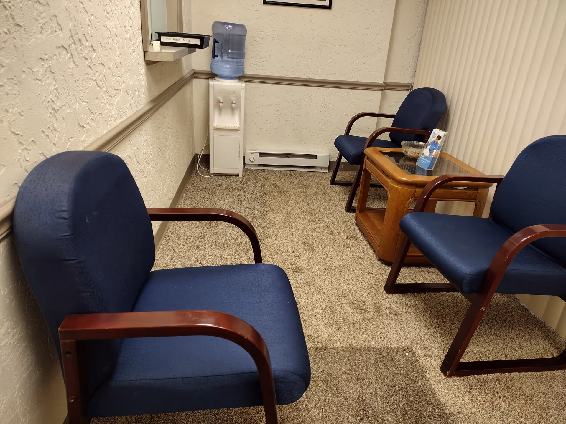 Small waiting area with blue chairs, a water cooler, and a wooden side table.