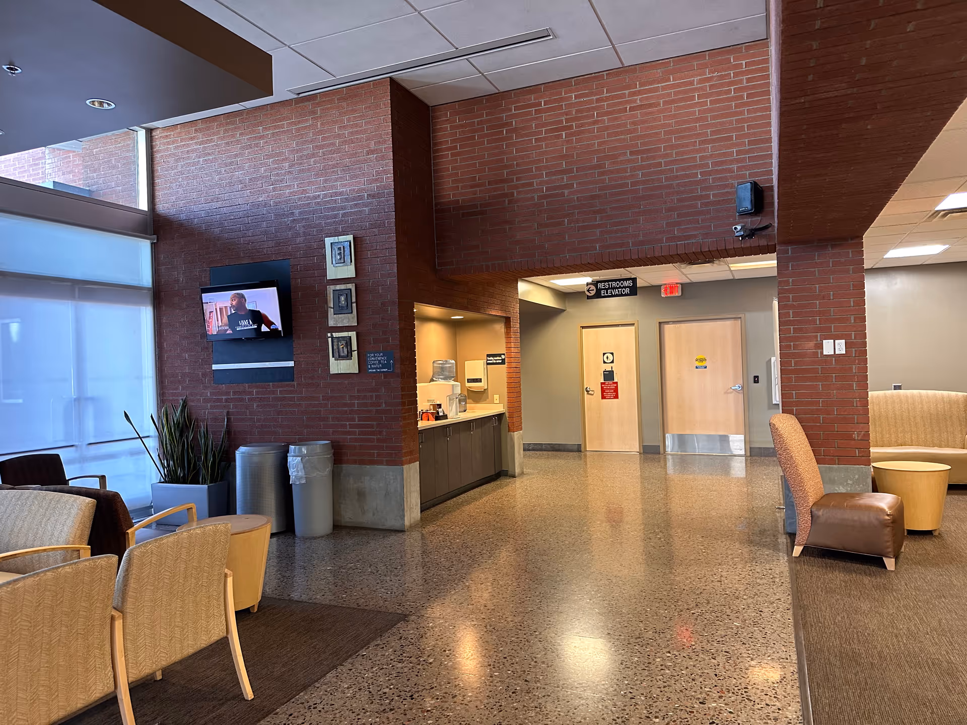 Interior hospital lobby with brick walls, seating area, a television, and a front desk.