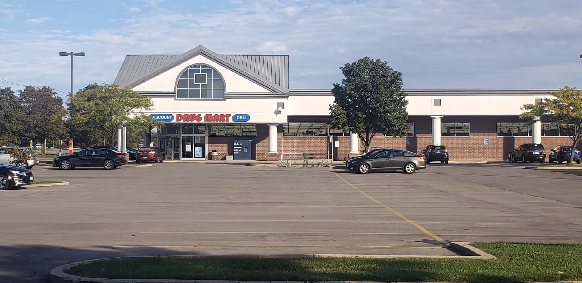 Front exterior of Discount Drug Mart with parking lot and a clear blue sky.