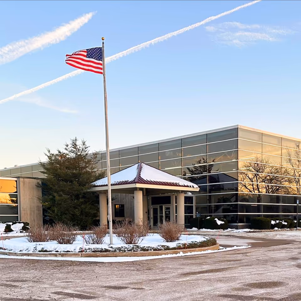 Exterior view of a modern facility with glass walls, flagpole, and snowy landscaping.