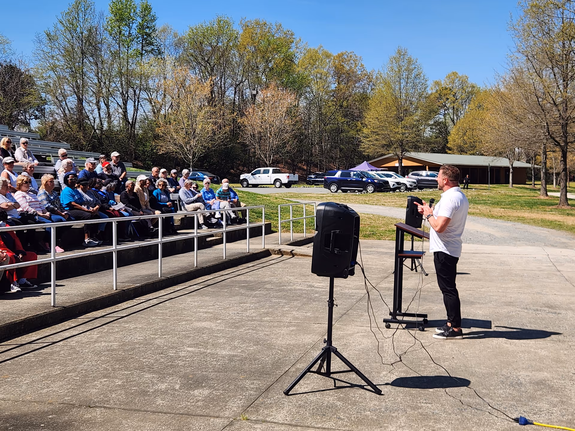Speaker addresses a seated outdoor audience of seniors at a Senior Helpers event.