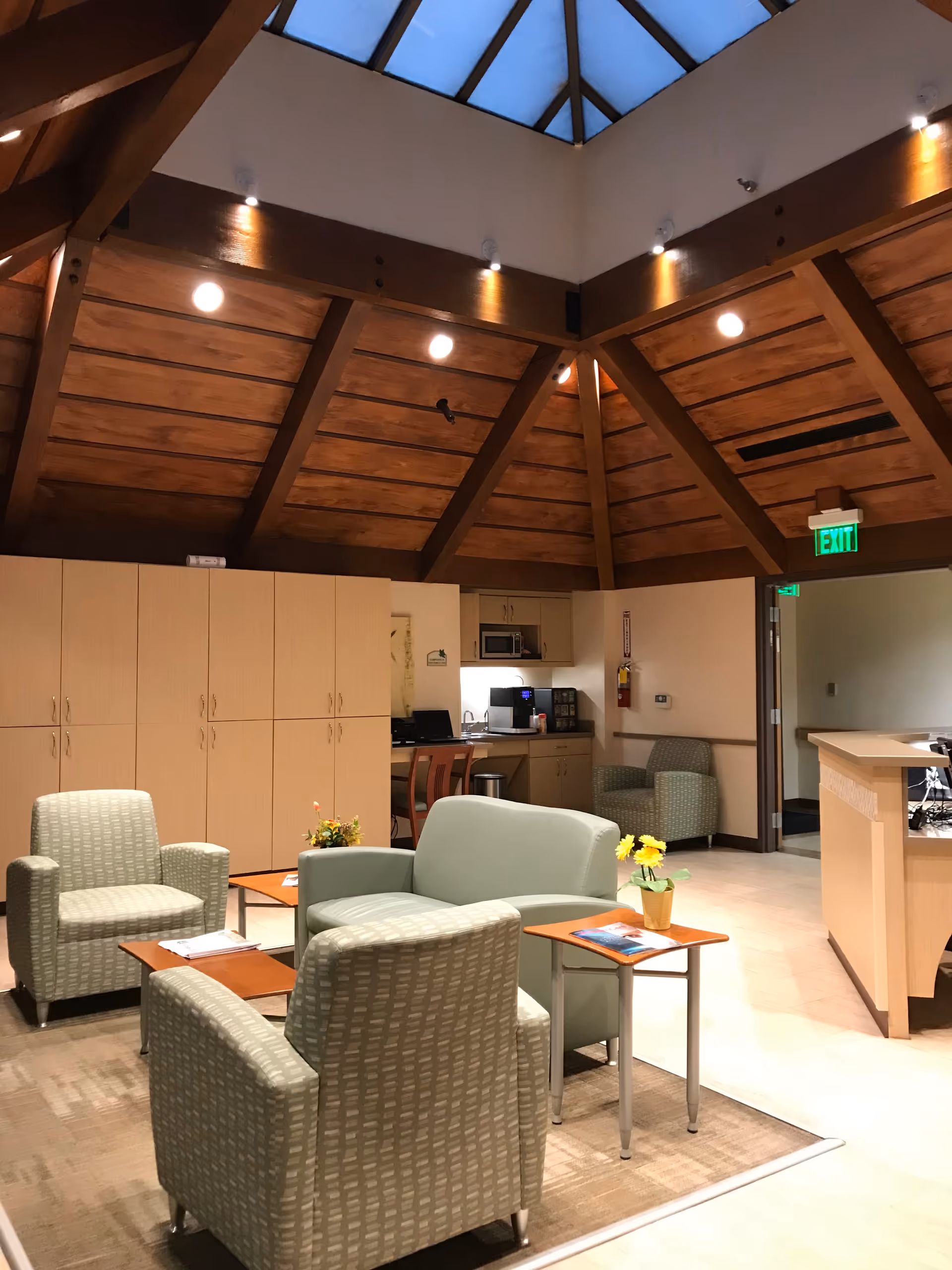 Interior living lounge with a wood-beam vaulted ceiling, beige seating, and a kitchenette in back.