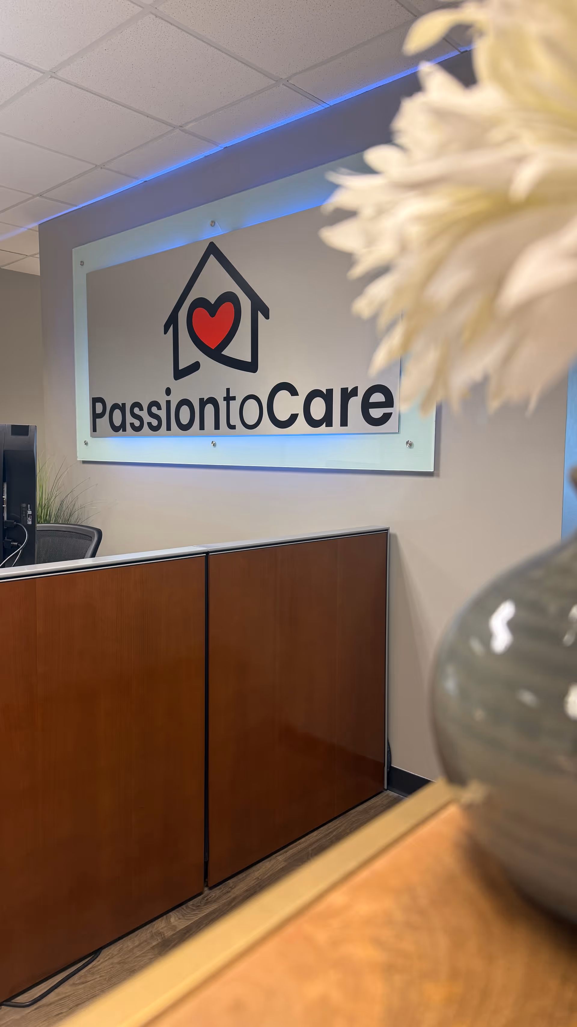 Interior reception area with PassiontoCare sign, wooden cabinets, and a blurred flower vase.
