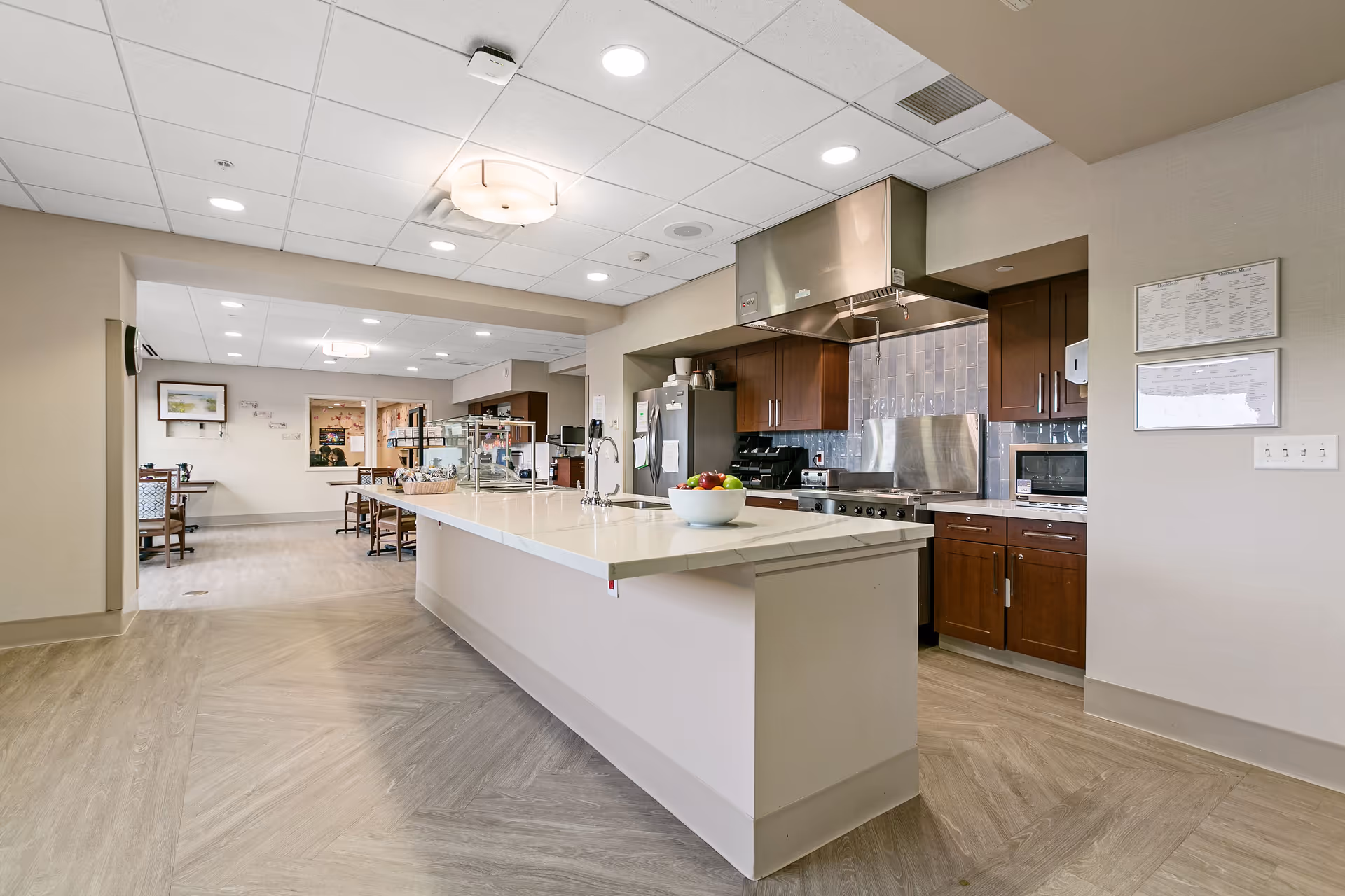 Senior living facility kitchen with central island, stainless appliances, and dining area in background