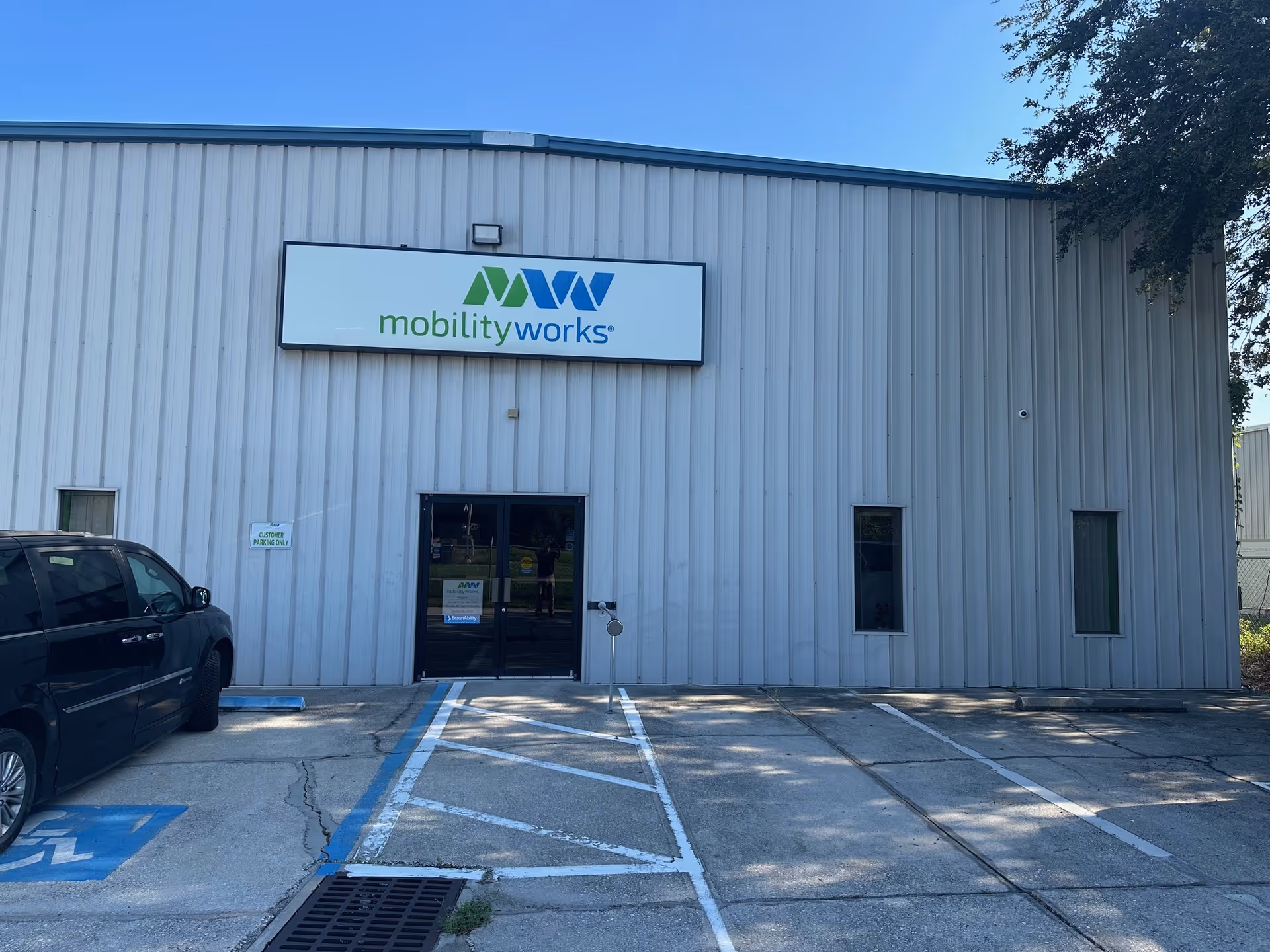 Exterior view of MobilityWorks building with sign, entrance doors, and parking lot in foreground.