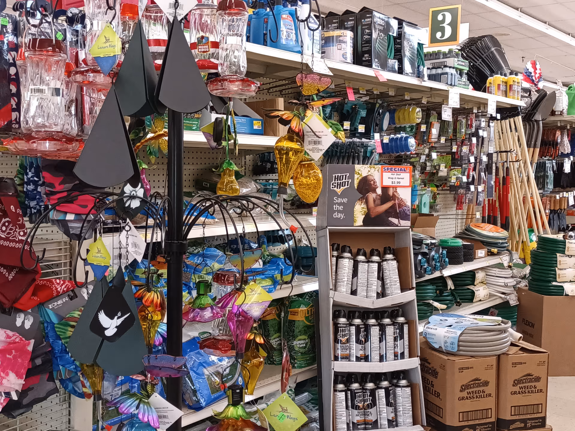 Interior store aisle densely stocked with gardening tools, watering cans, hoses, and assorted merchandise.