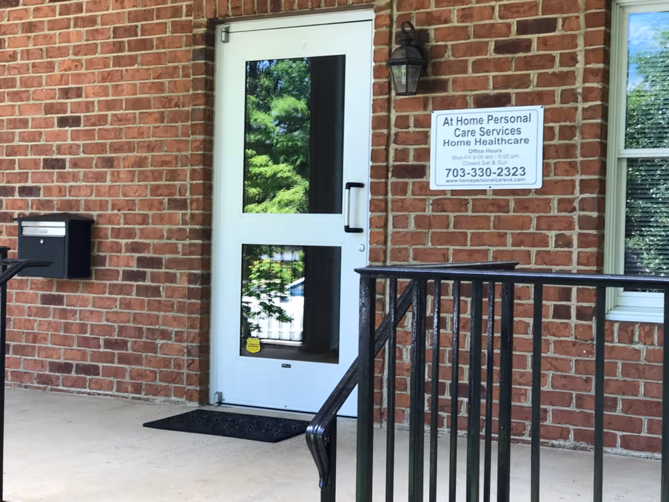 Brick building exterior with a white door, sign, mailbox, and railing.