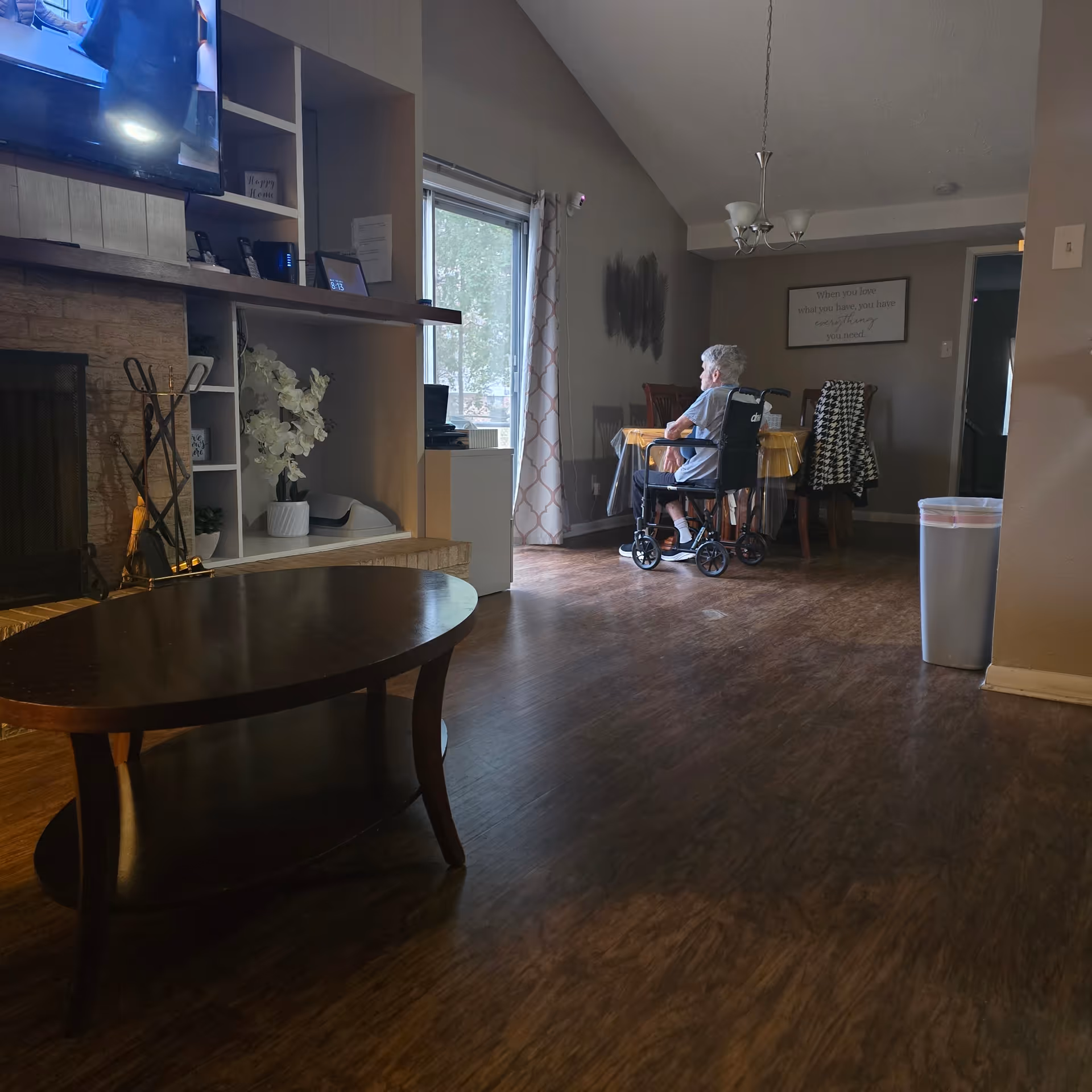 Senior resident in a wheelchair sits at a dining table in a cozy living area.