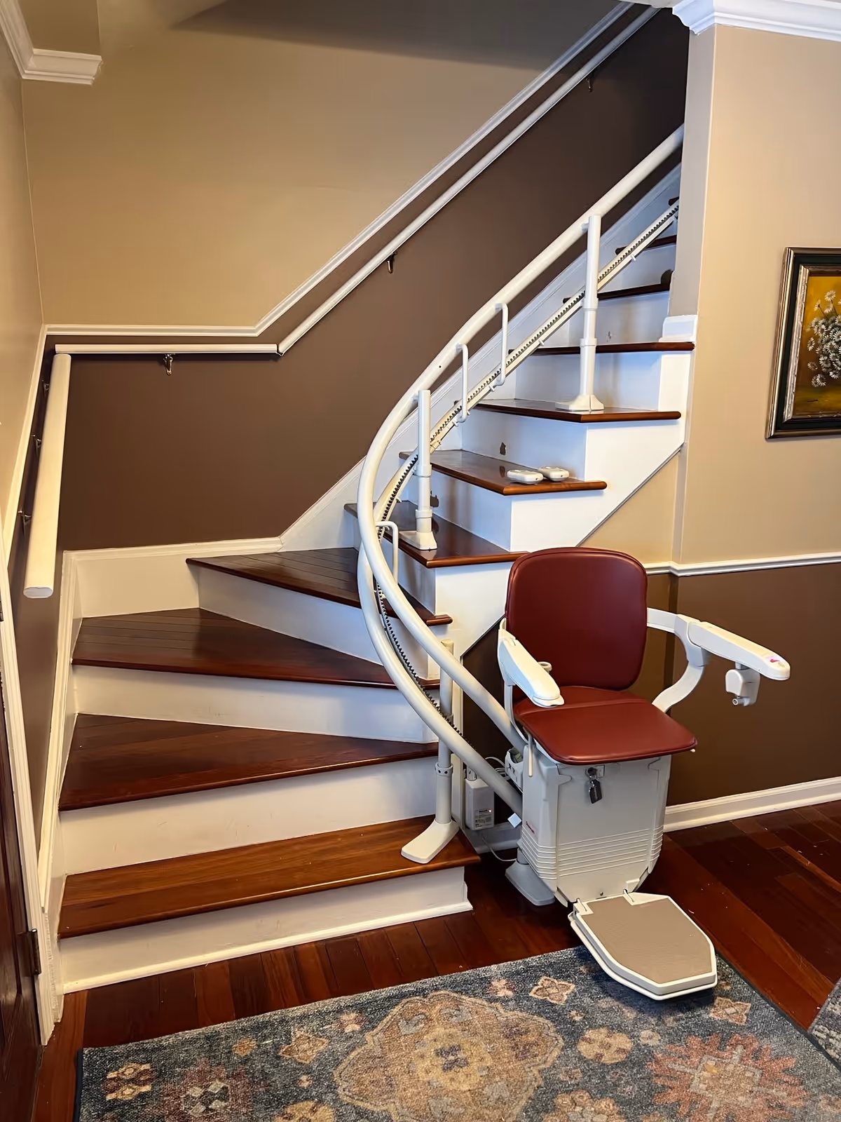 Indoor staircase with a white curved chairlift and burgundy seat in a home interior.