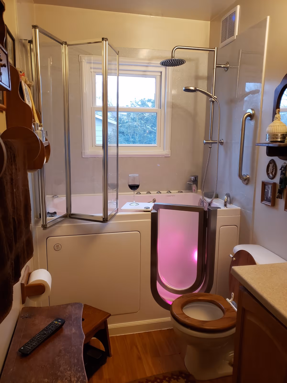 A bathroom with a pink-lit walk-in tub, glass shower enclosure, toilet, and window.