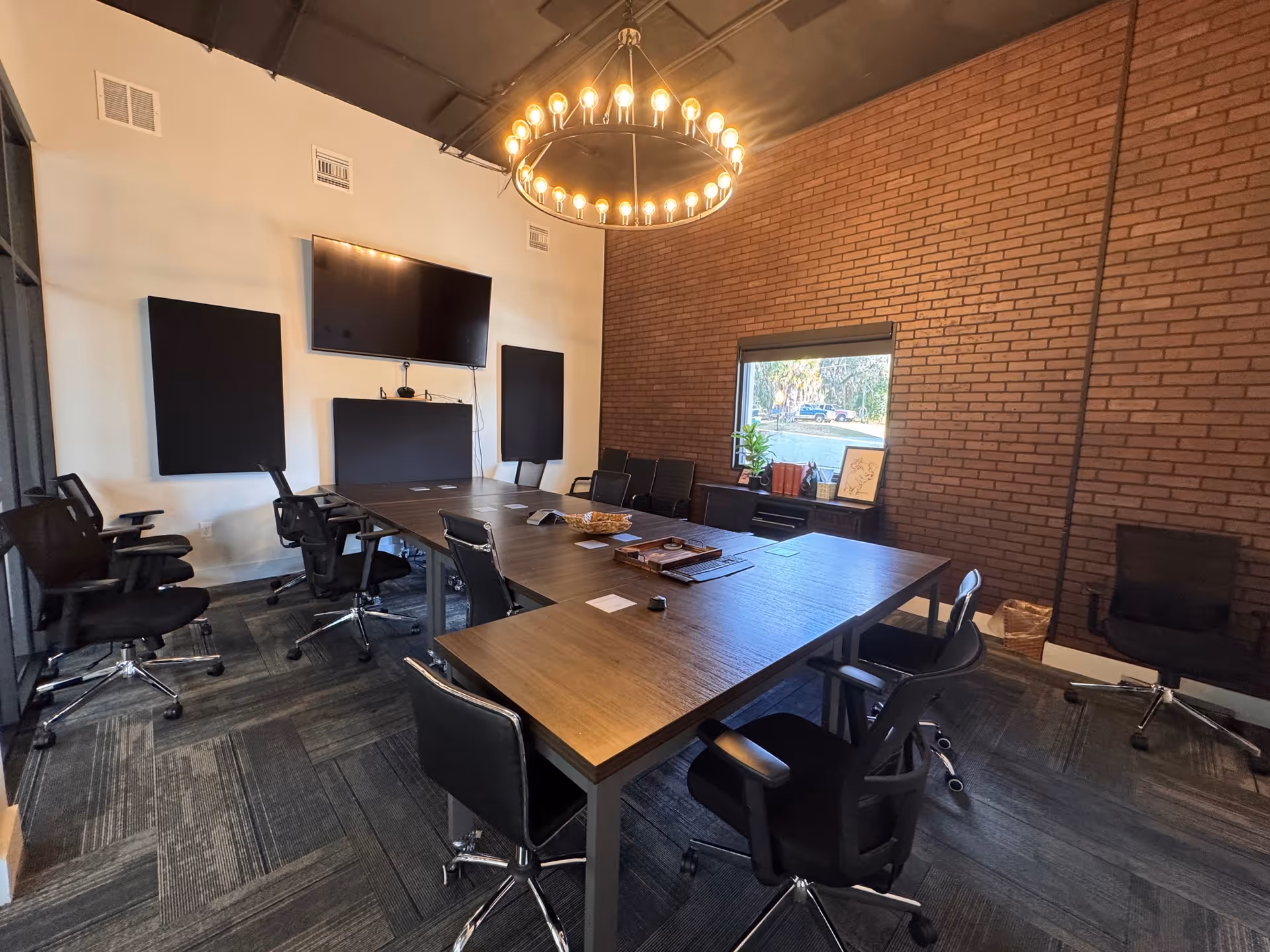A modern conference room with a large table, black chairs, a wall-mounted screen, and brick walls.
