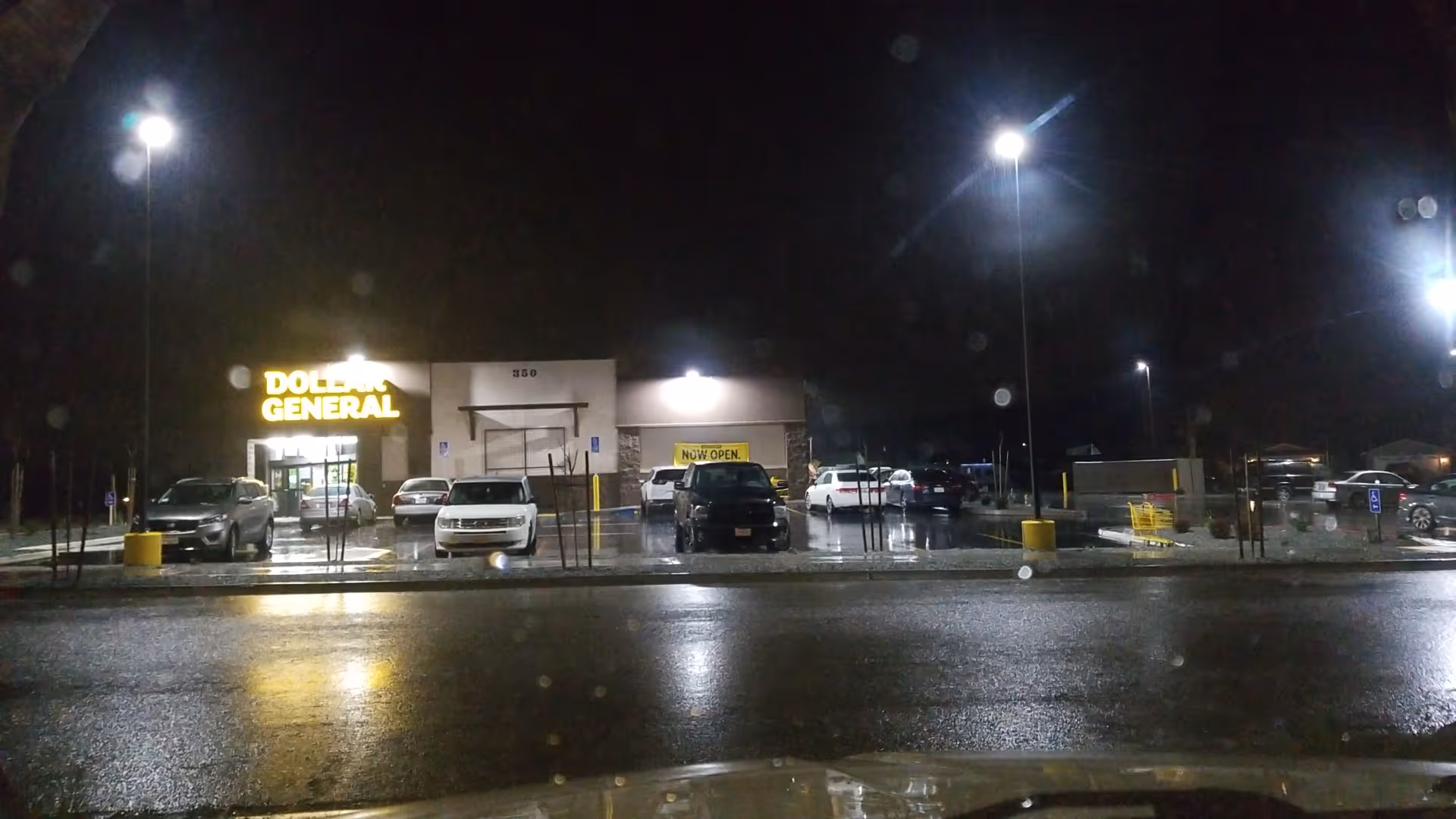 Nighttime exterior view of a Dollar General storefront with a wet parking lot and cars.