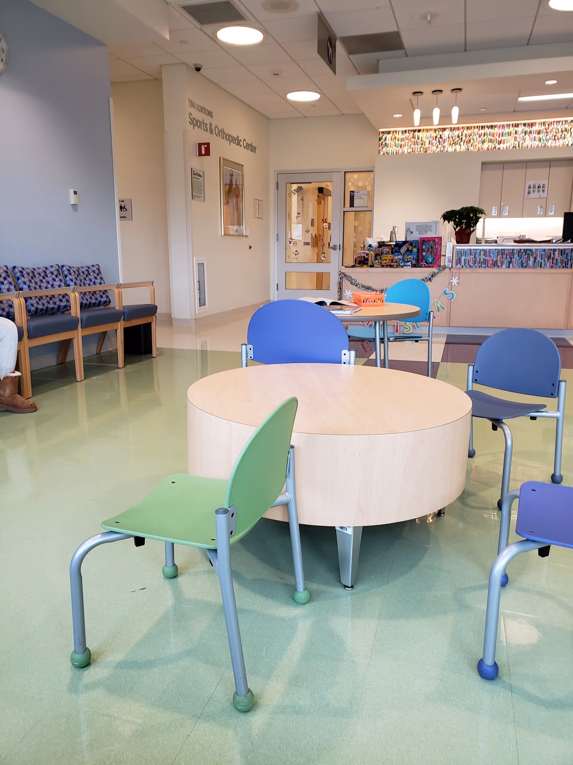 A bright pediatric clinic waiting area with a round table and colorful chairs.