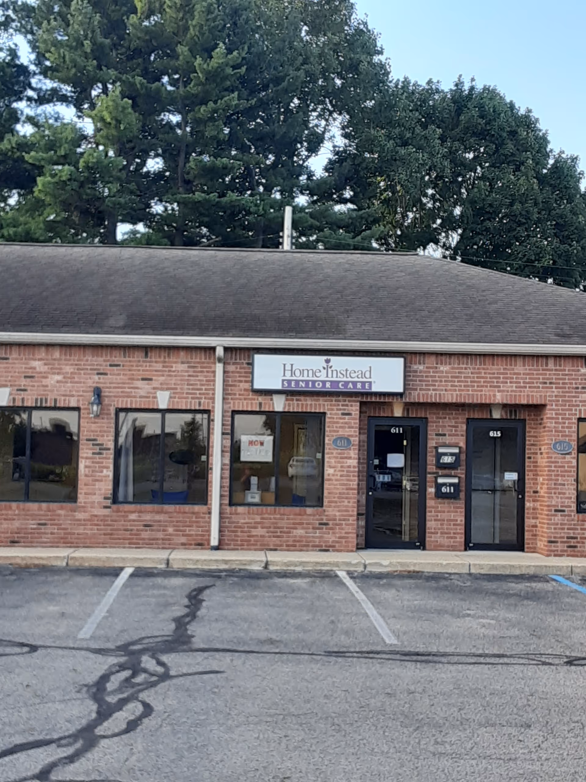Brick building storefront with Home Instead Senior Care sign and parking lot in front.