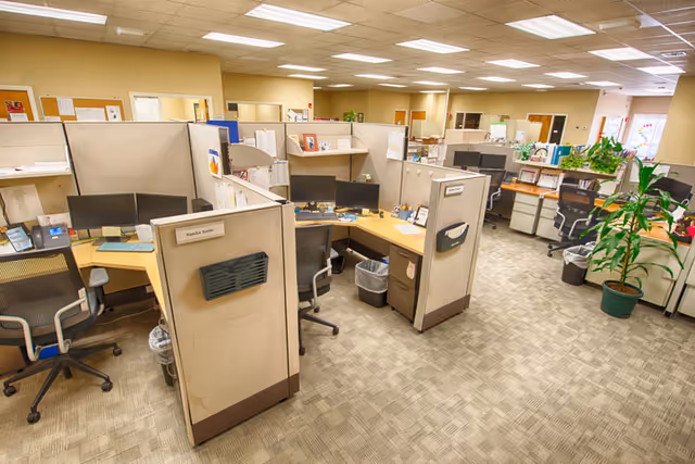 A spacious office with cubicles, desks, computers, and chairs inside a senior care facility.