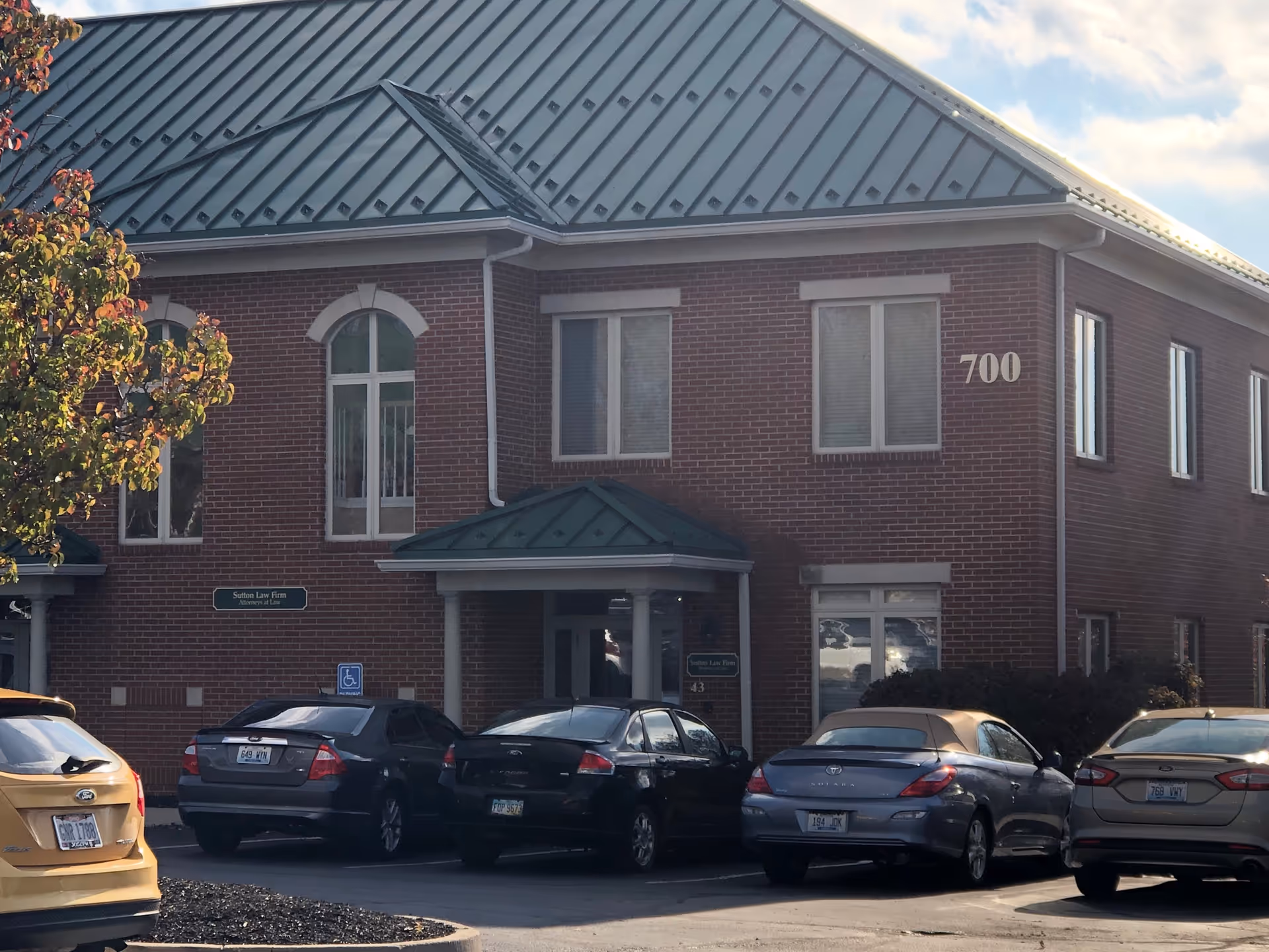 Brick building with green metal roof and the number 700, cars parked in front