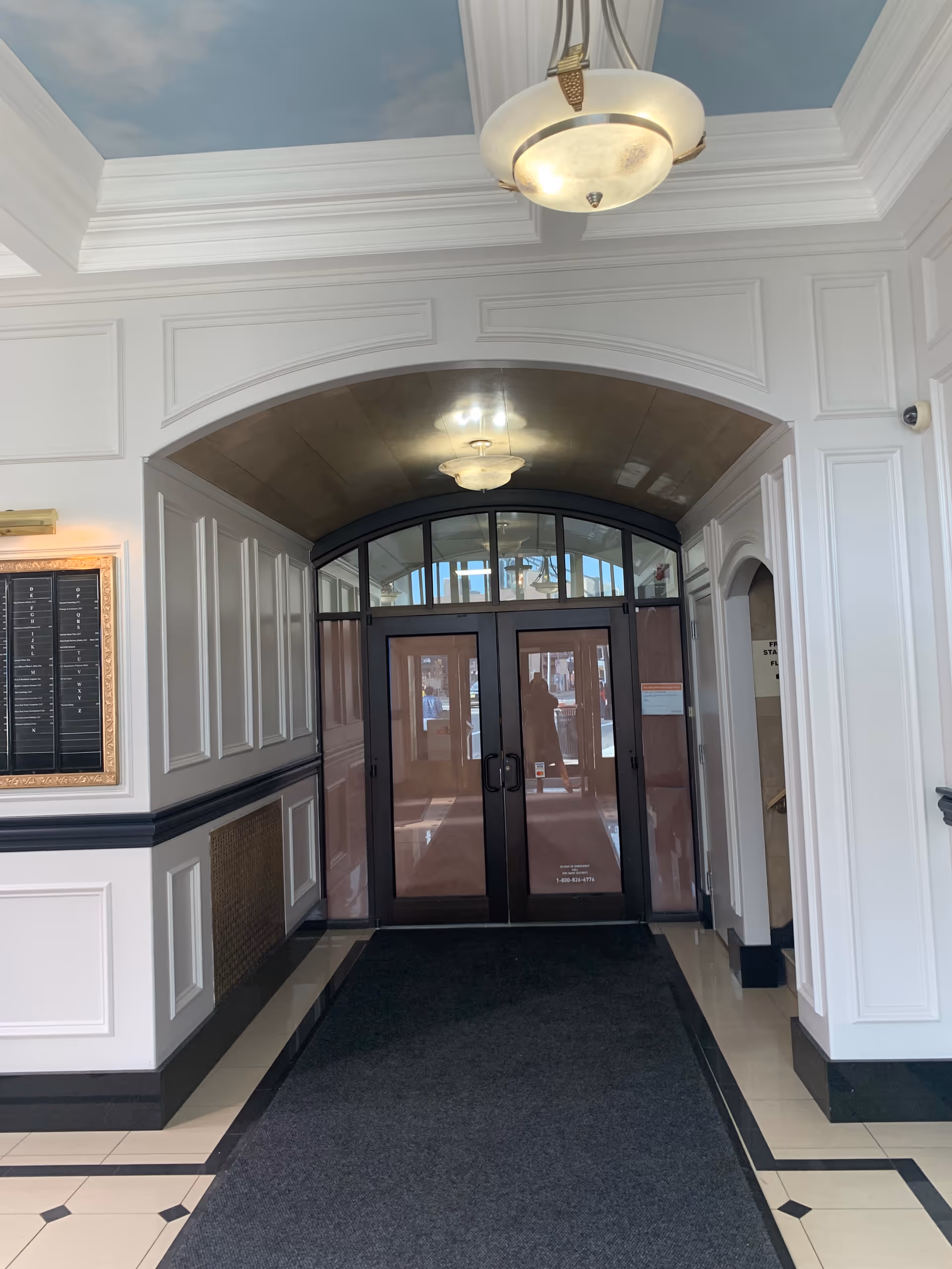 Elegant lobby entrance with arched doorway, double glass doors, chandeliers, and decorative paneling.